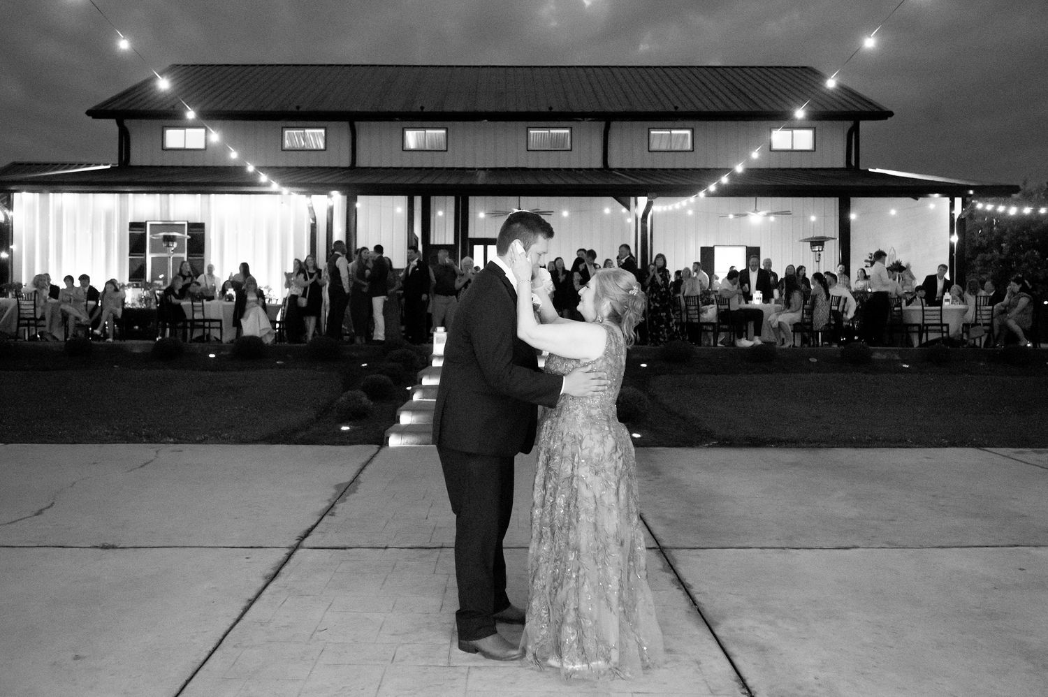 Black and white photo of a couple sharing their first dance outdoors at an elegant evening wedding reception.