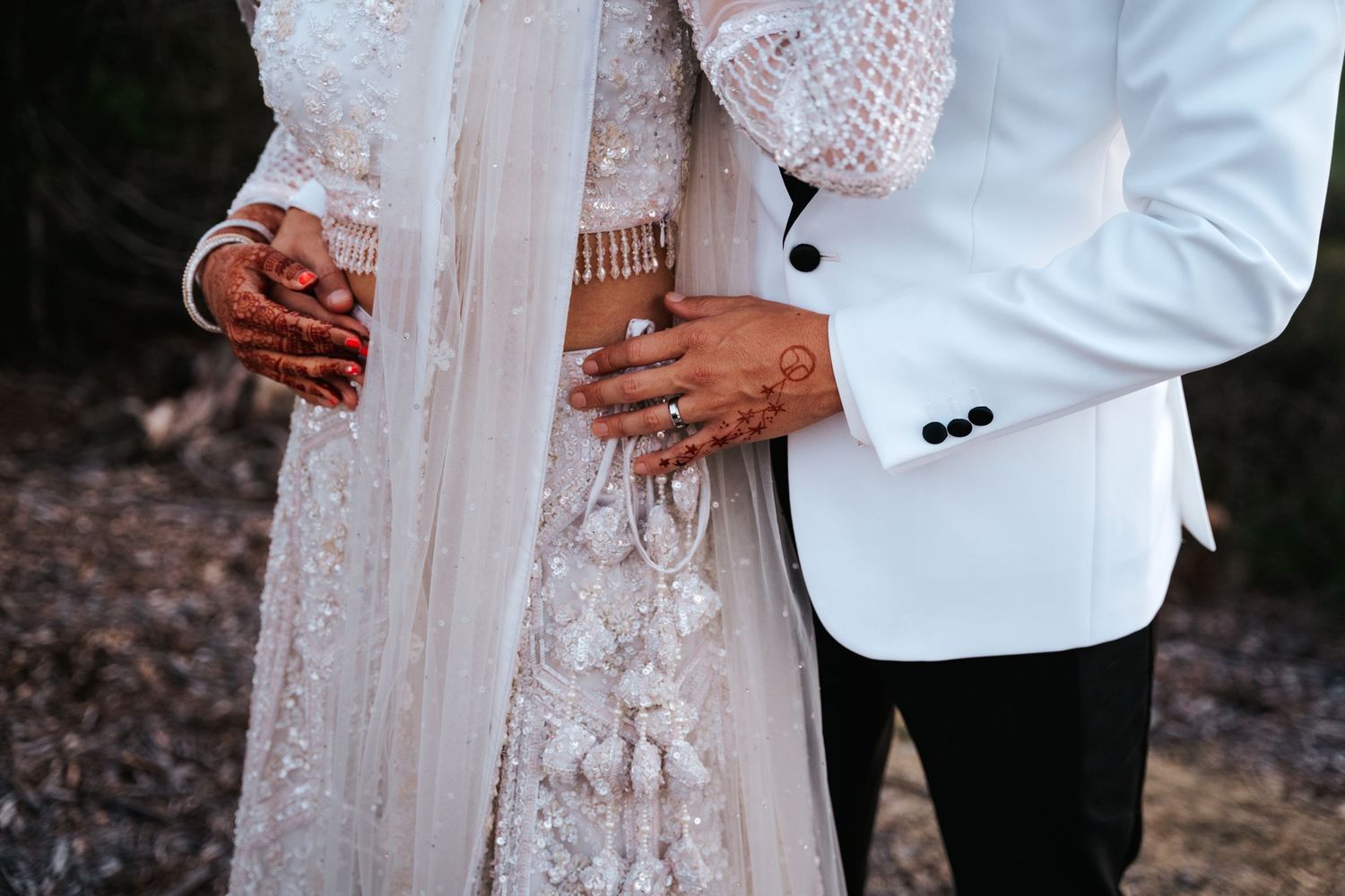 Couple walks down aisle in traditional Indian wedding attire at outdoor ceremony with guests and floral decorations.