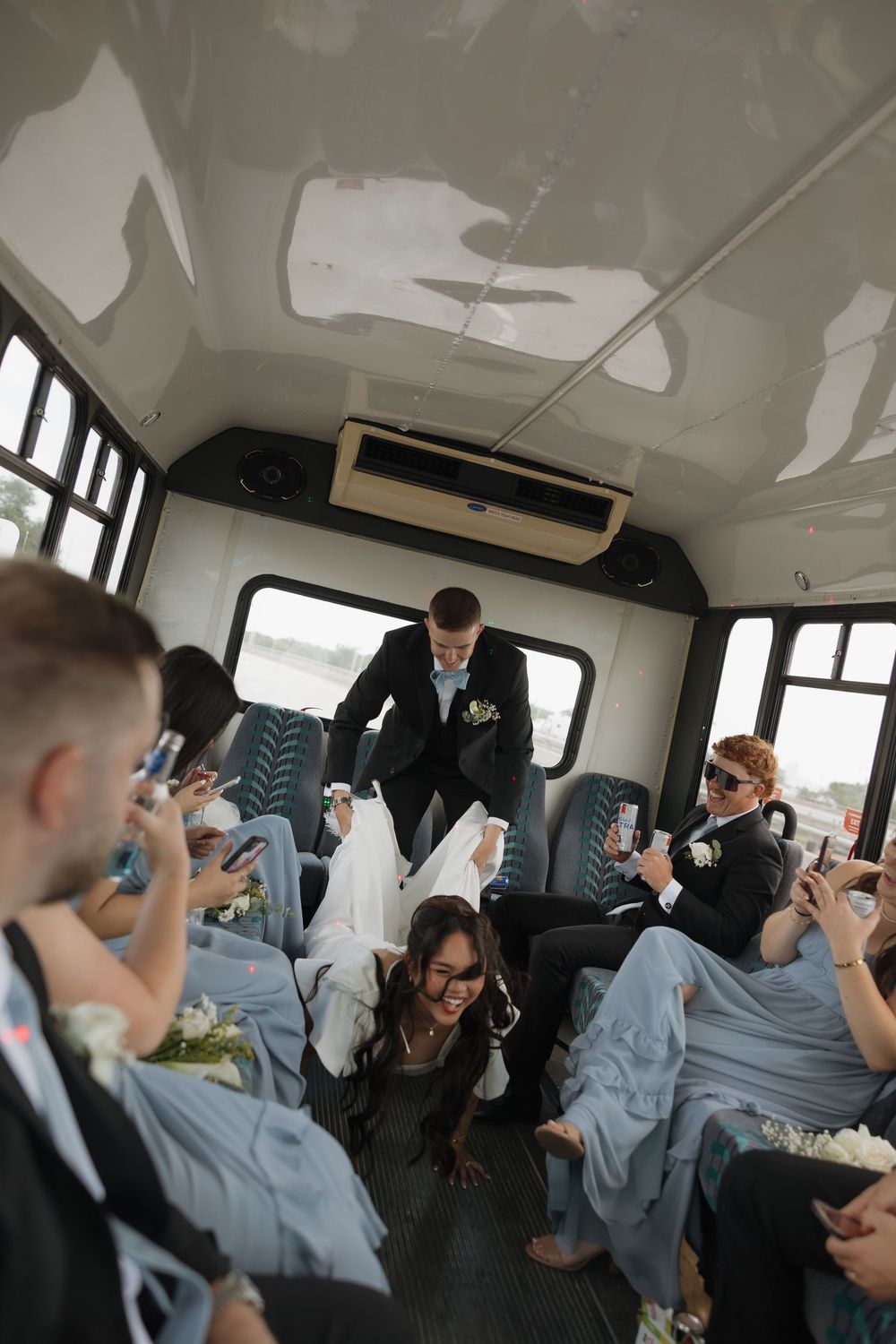 Wedding party celebrates on a party bus as bride and groom share a fun moment with cheering guests.
