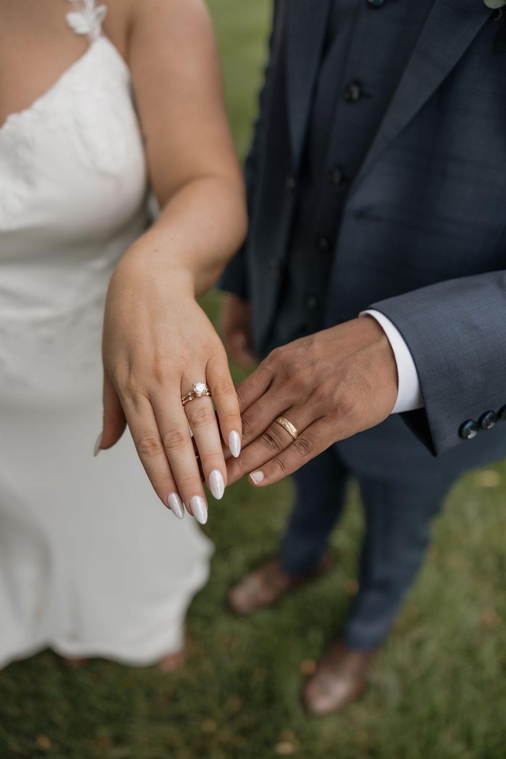 Close-up of bride and groom displaying gold wedding rings and diamond engagement ring on their hands.
