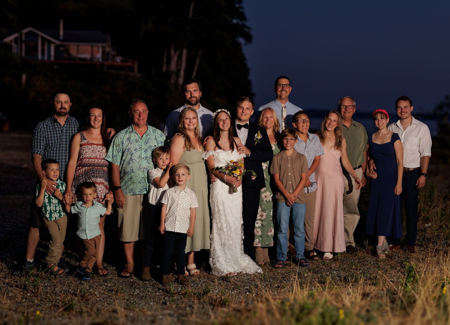 Large wedding party group photo taken outdoors near the waterfront at dusk.