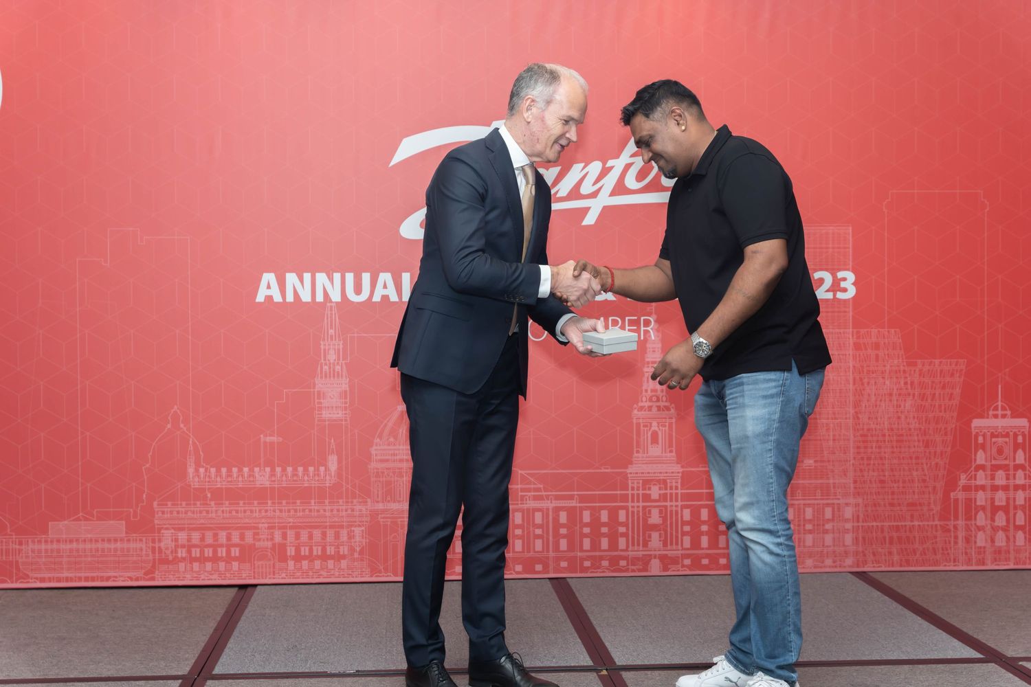 Corporate award presentation ceremony against a red branded backdrop at an annual event.