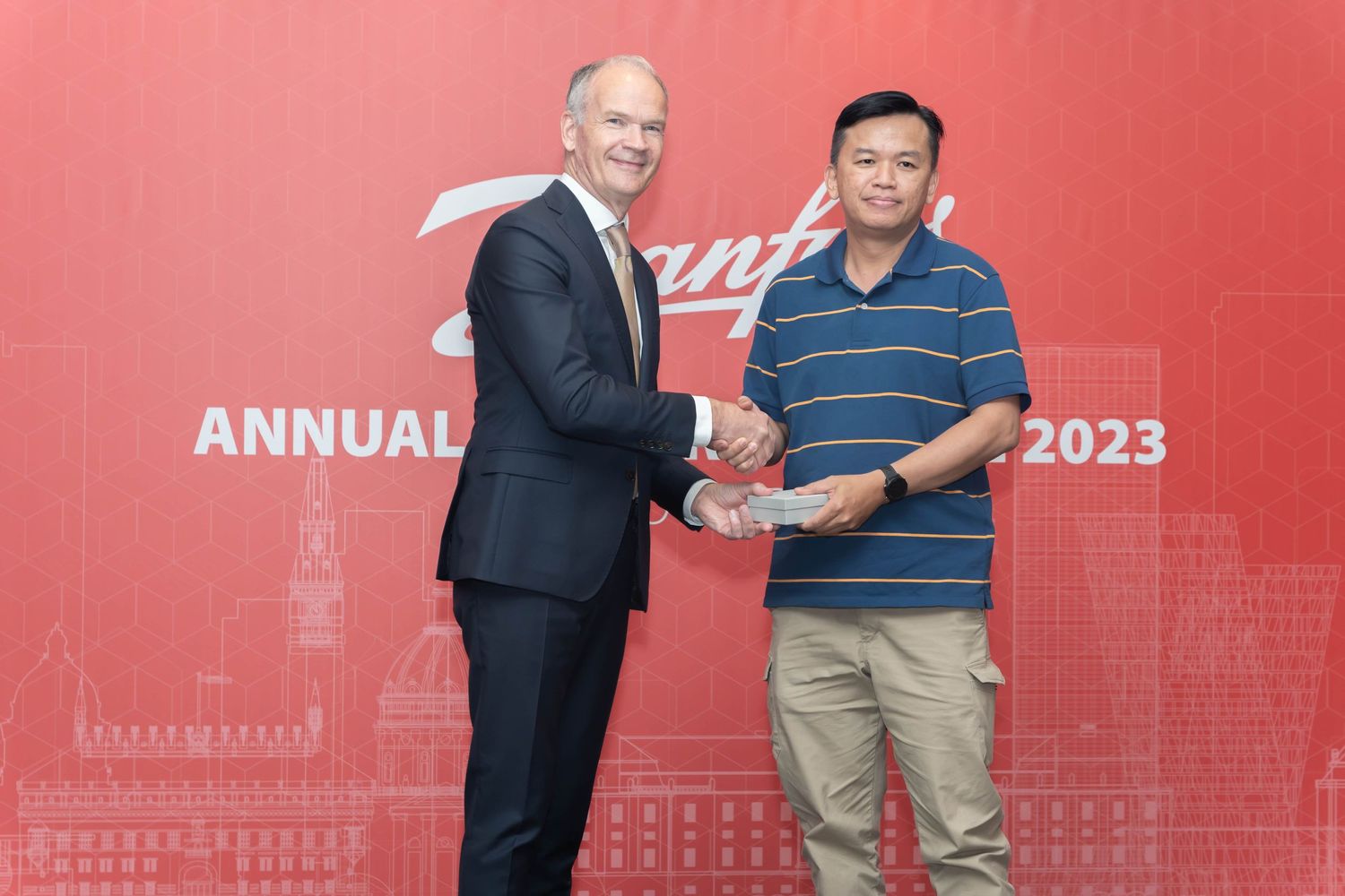 Professional award handshake and photo opportunity in front of red company backdrop.