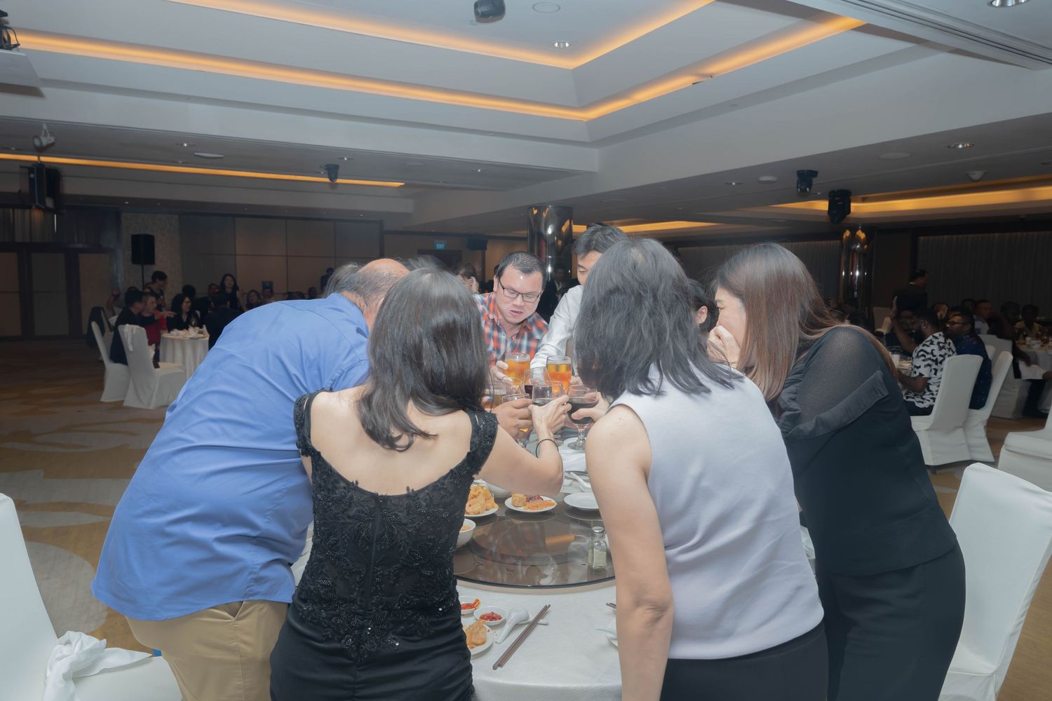Group of attendees gathered closely around table during social event in banquet setting.