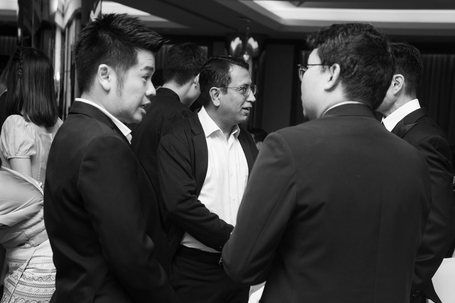 Black and white photo of business people in suits having a conversation at formal event.