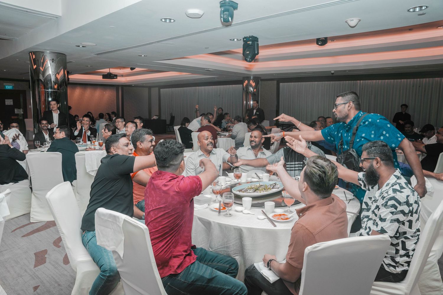 Lively group dinner celebration with guests interacting around circular tables in banquet hall.