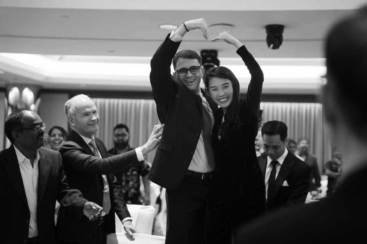Black and white photo of celebratory moment with raised arms at formal business gathering.