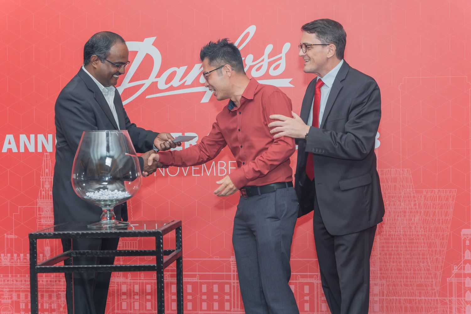 Three people participating in a ceremony with a glass trophy at Danfoss event.