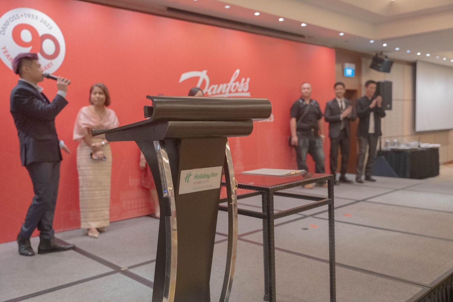 Corporate event setup with podium and speakers against red wall displaying Danfoss branding.