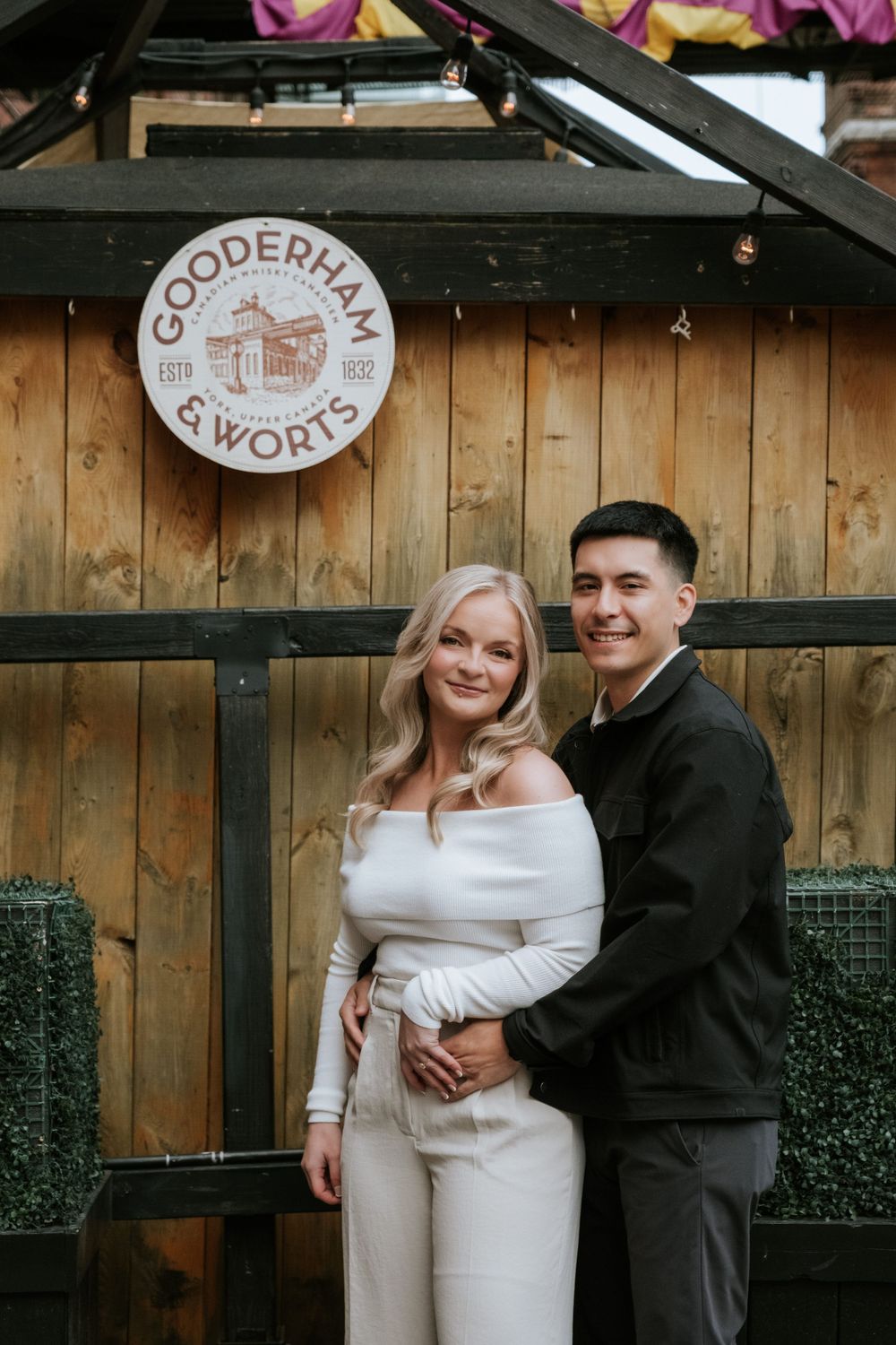 A sweet moment shared in front of a rustic wooden wall with Gooderham & Worts signage.