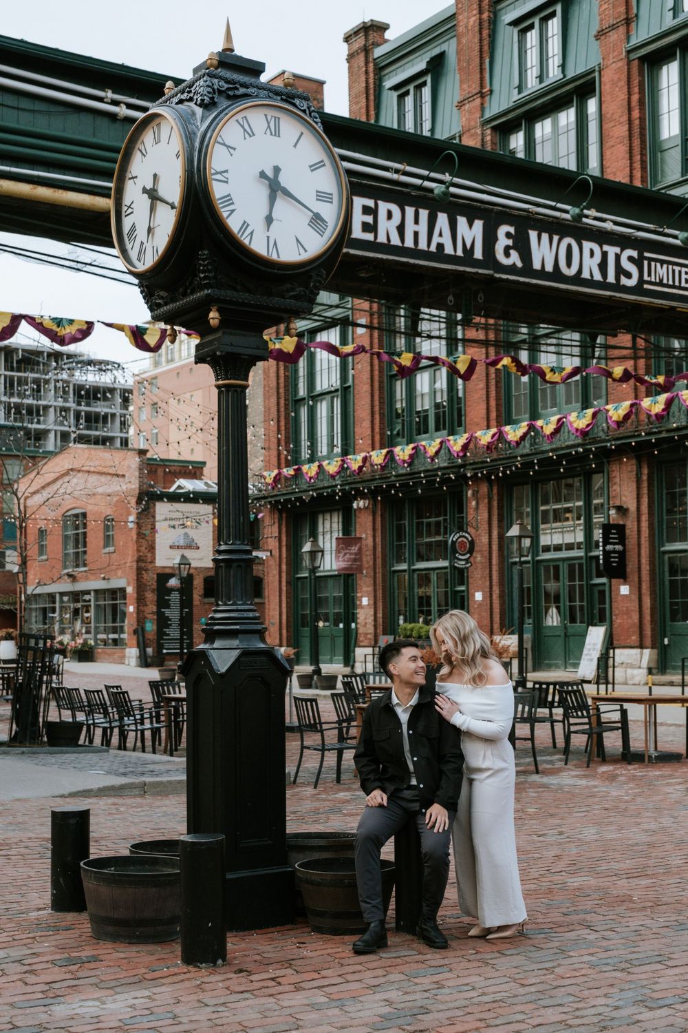 A vintage clock tower with Erham & Worts Limited signage stands over a brick plaza with outdoor seating.