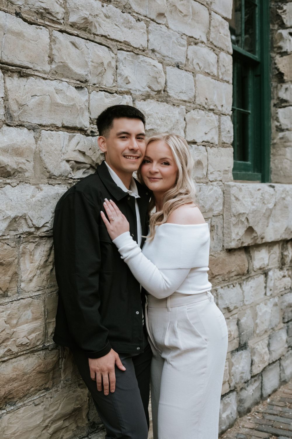 Romantic couple in formal wear posing against stone wall exterior.