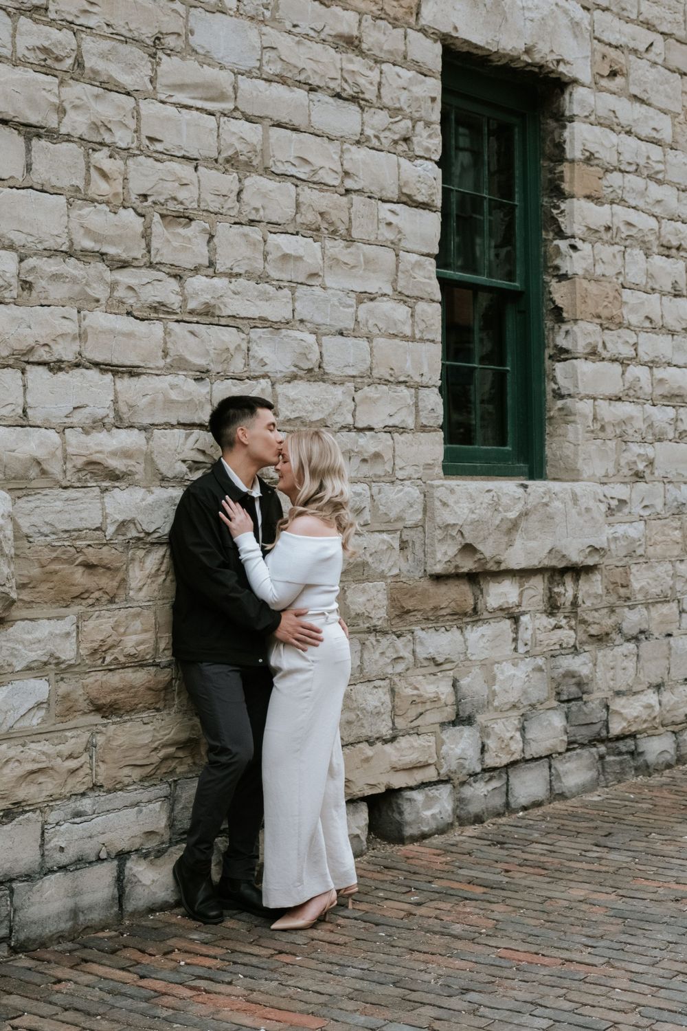 A romantic moment captured against a stone wall with green window frames.