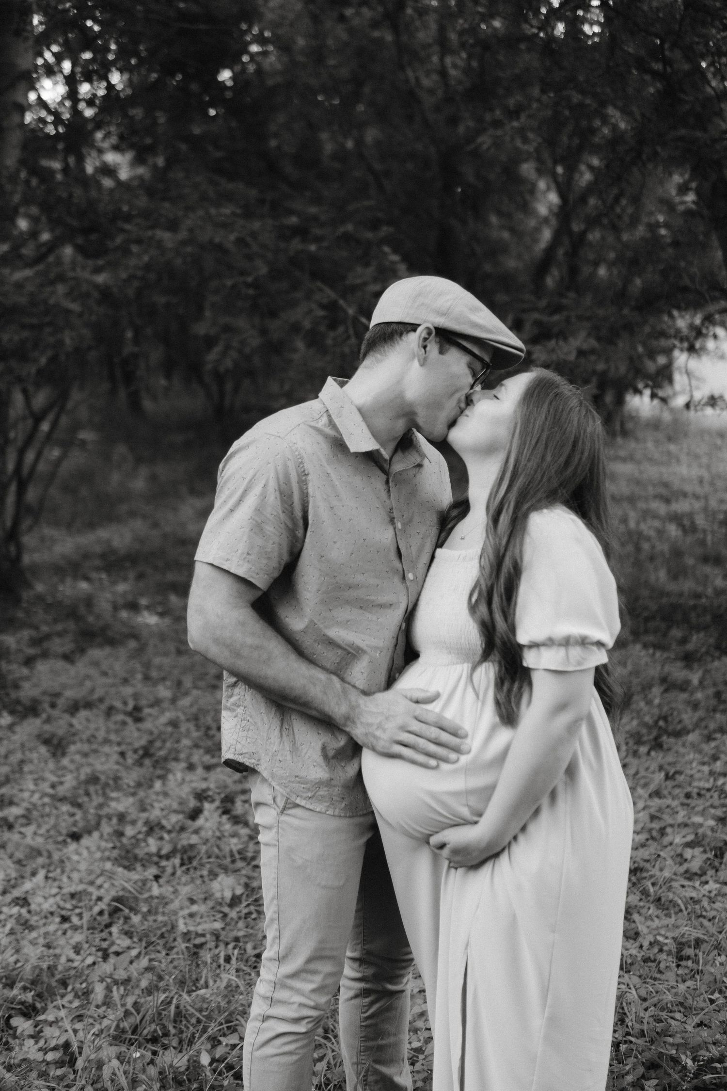 Photo of an expecting couple embracing outdoors, with the mother wearing a flowing white dress excited to welcome their little one.