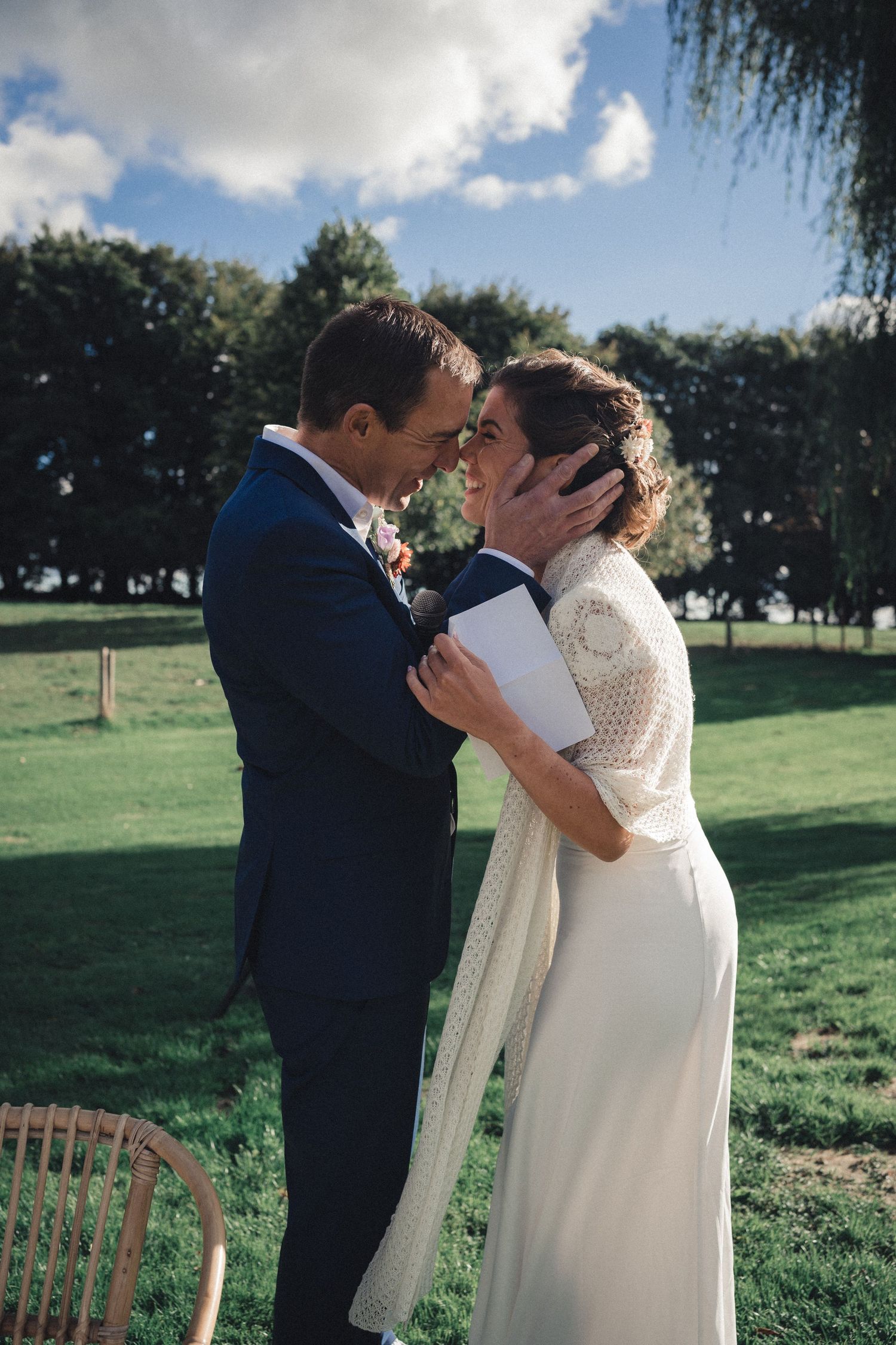An intimate wedding moment outdoors with a couple in formal attire sharing a tender embrace on a grassy lawn.