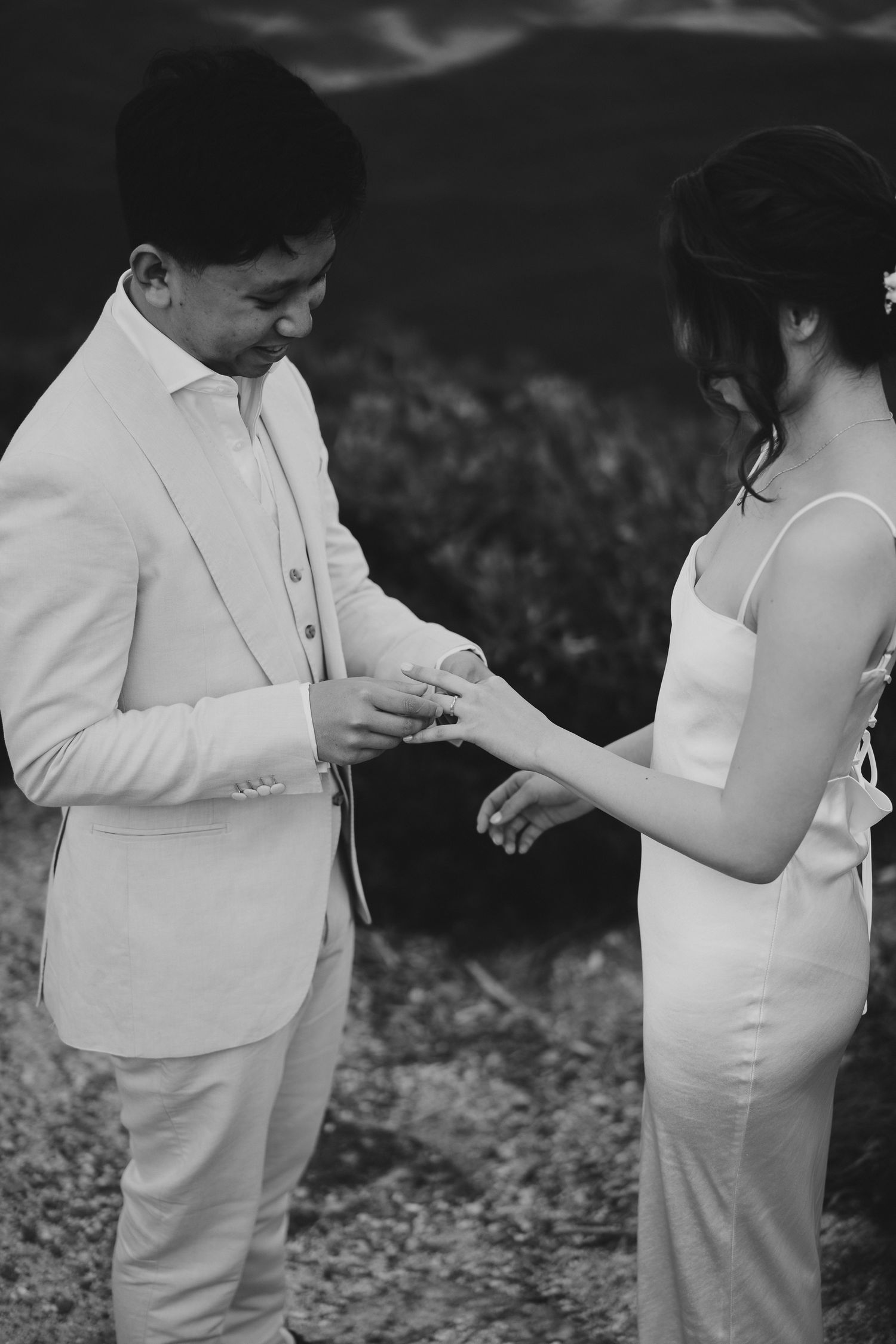 An intimate ring exchange moment captured in black and white against a mountain backdrop.