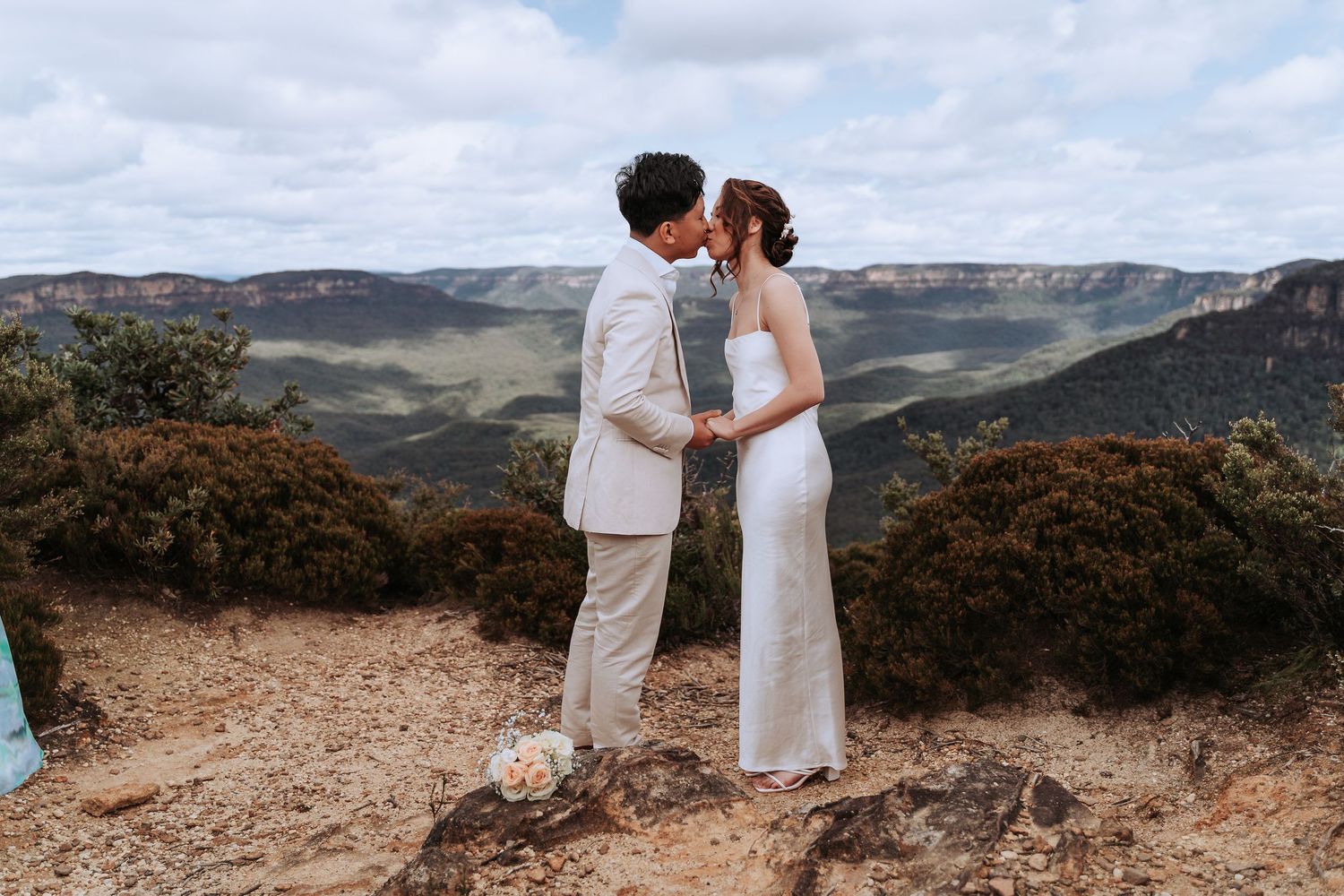 A romantic moment shared between a couple in white attire on a mountain overlook.