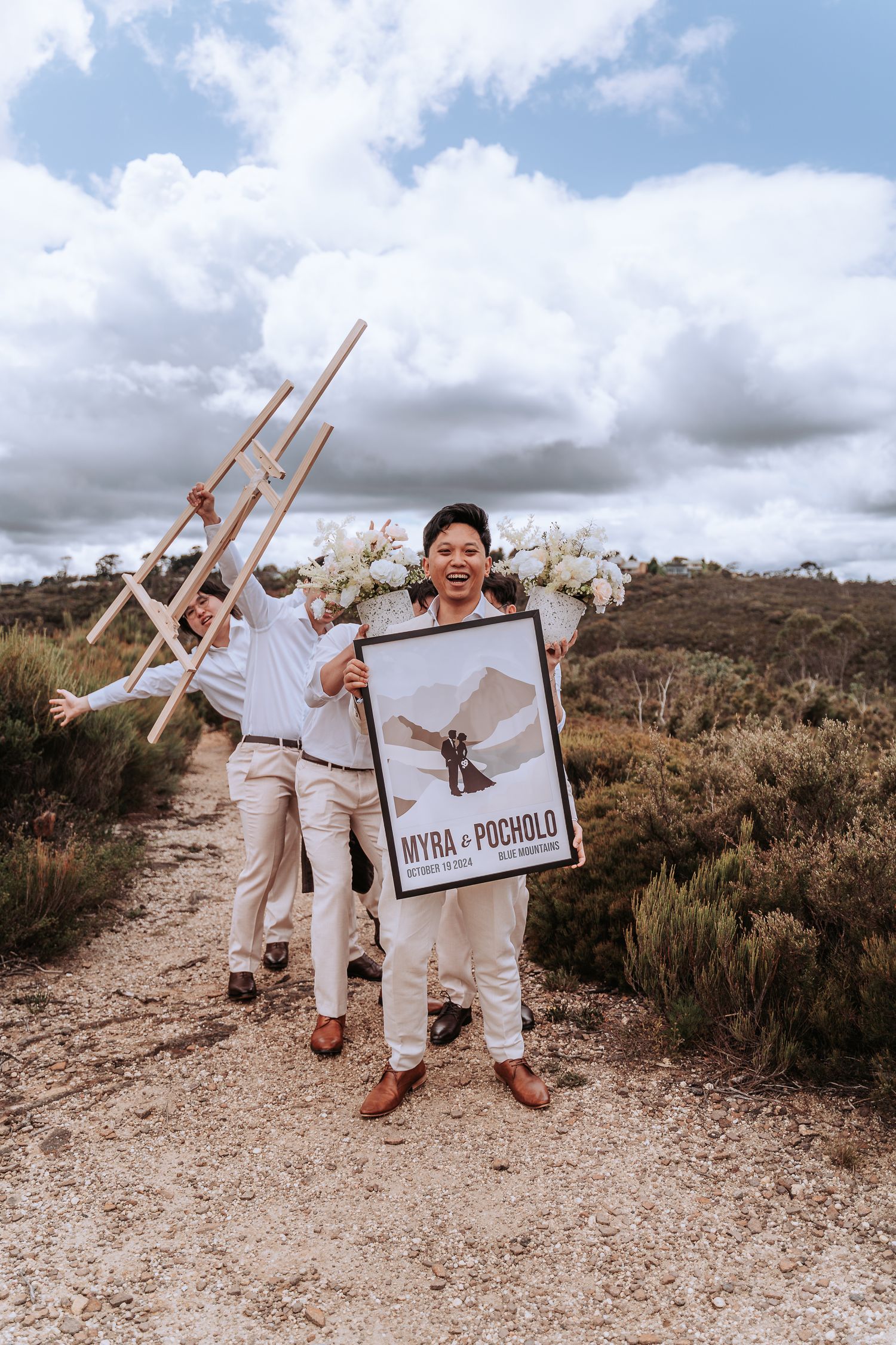 Group holding props and signage on a scenic mountain trail with cloudy sky.