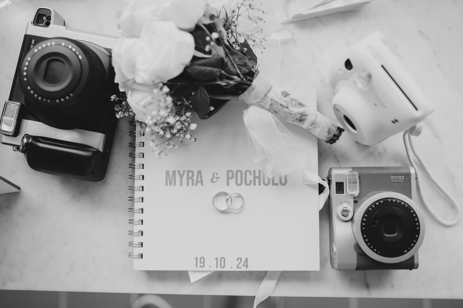 Flat lay of vintage cameras, notebook, and floral elements on white surface.
