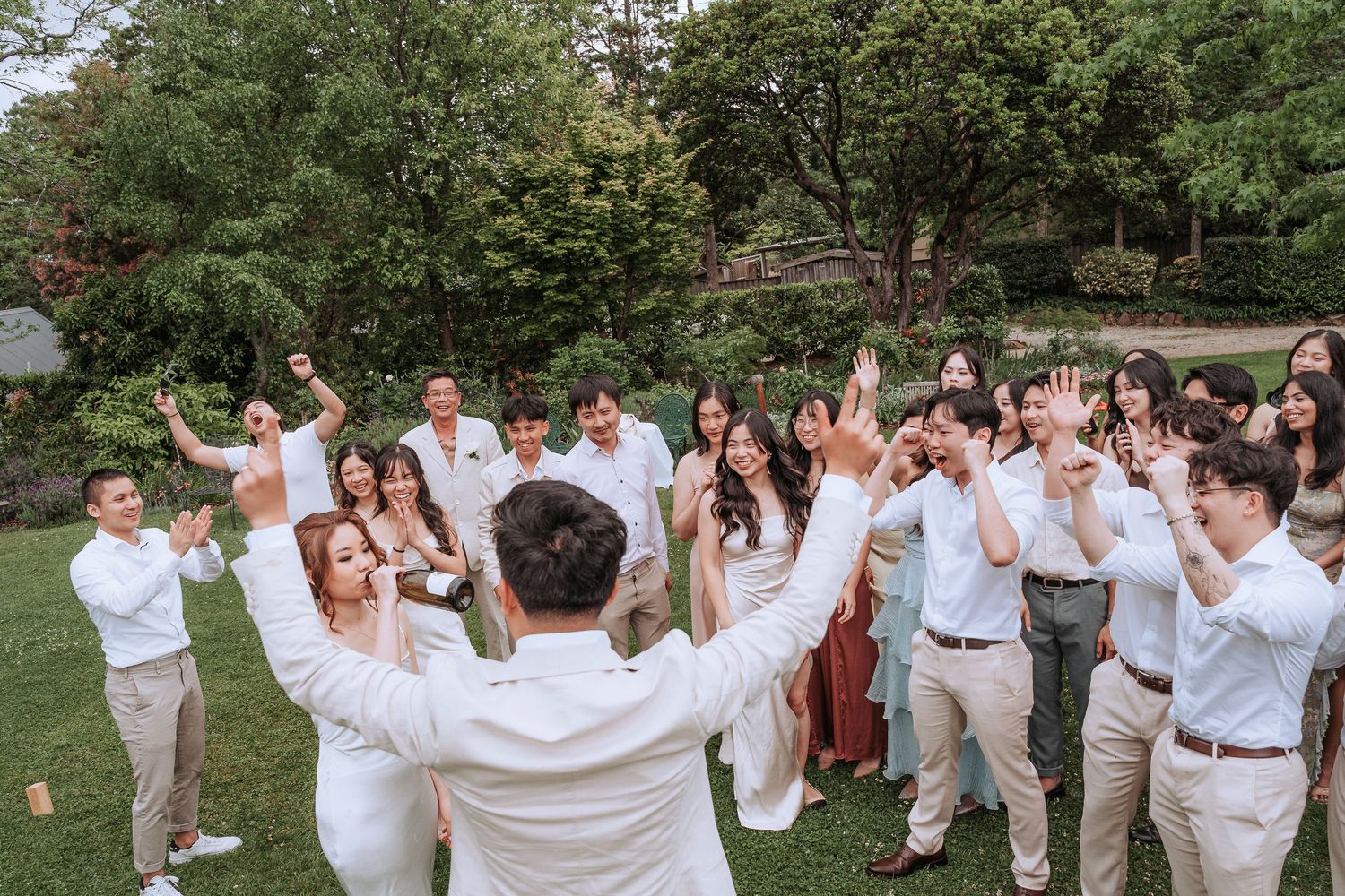 Celebration group photo with guests in coordinated white and beige outfits in a garden setting.