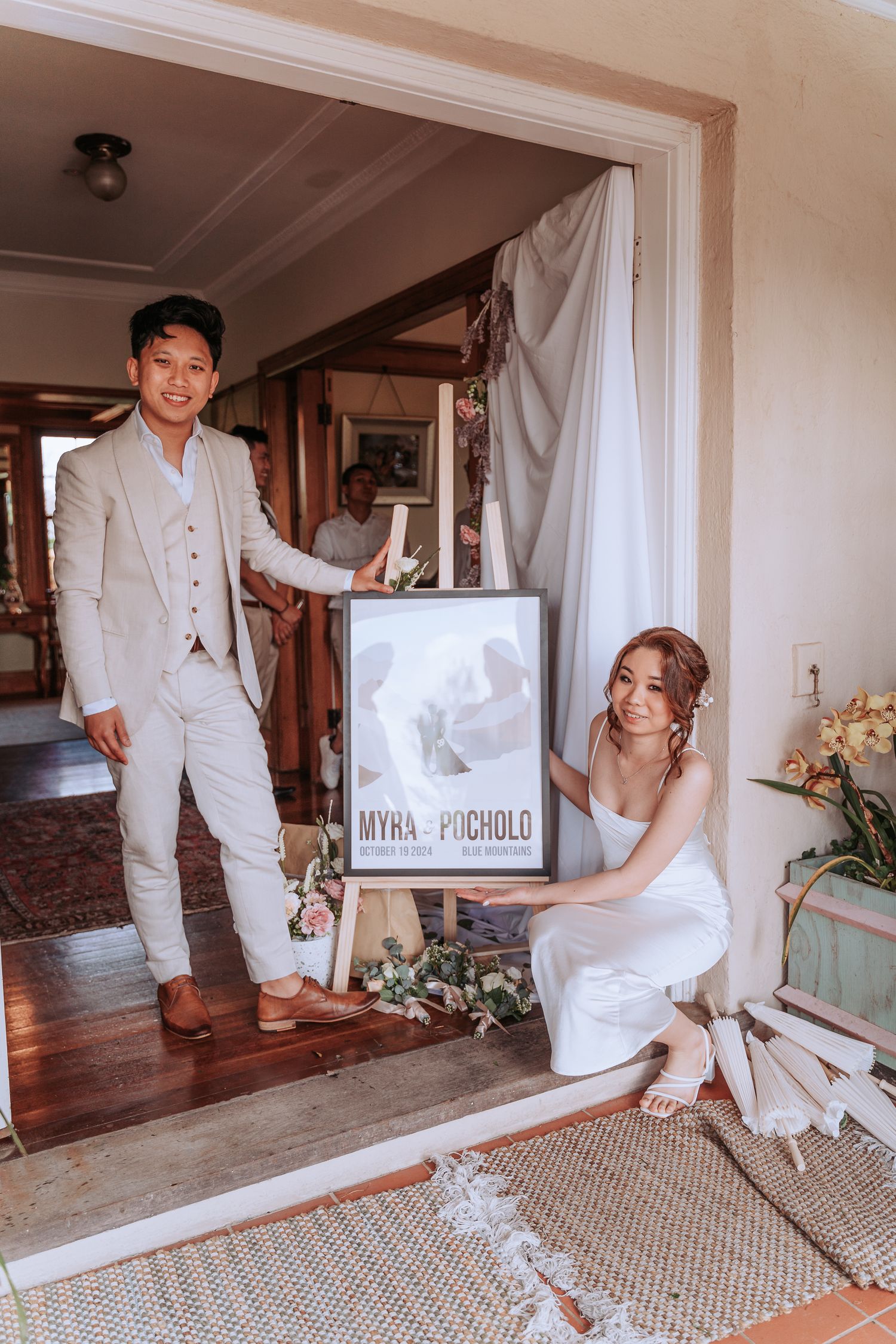 Couple poses with framed artwork in an elegant indoor setting.