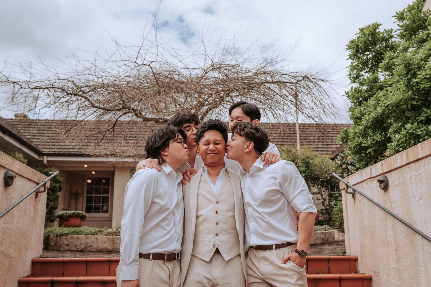 Three people share a warm moment on stone steps with brick building backdrop.
