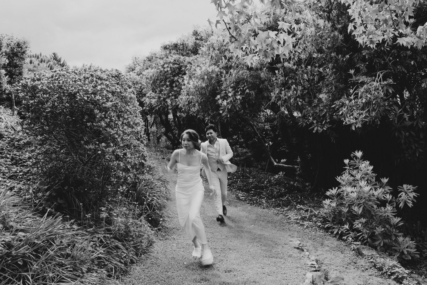 Couple runs joyfully down a garden path in black and white.