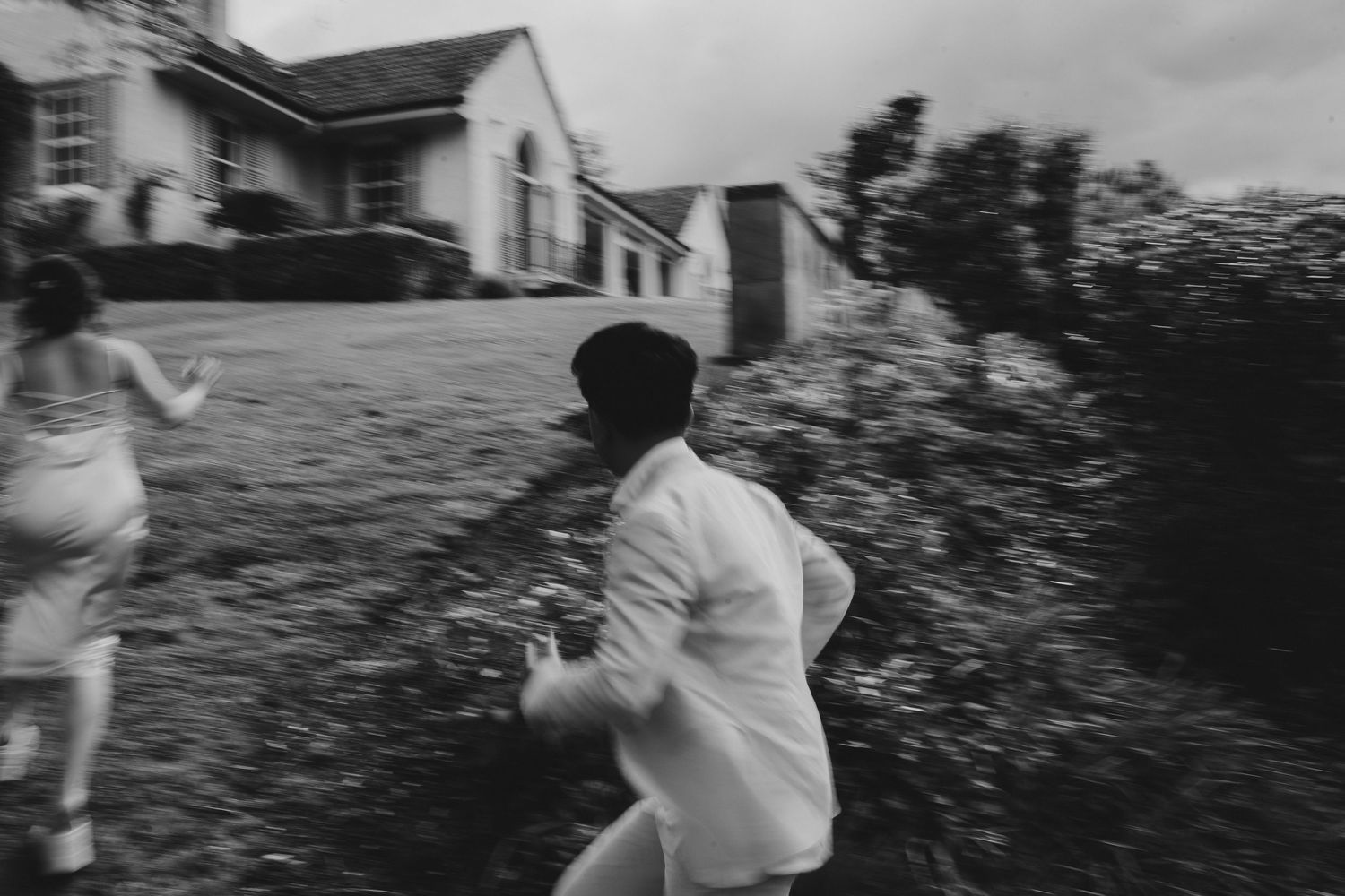 Motion-blurred figures in white clothing running outside a house.