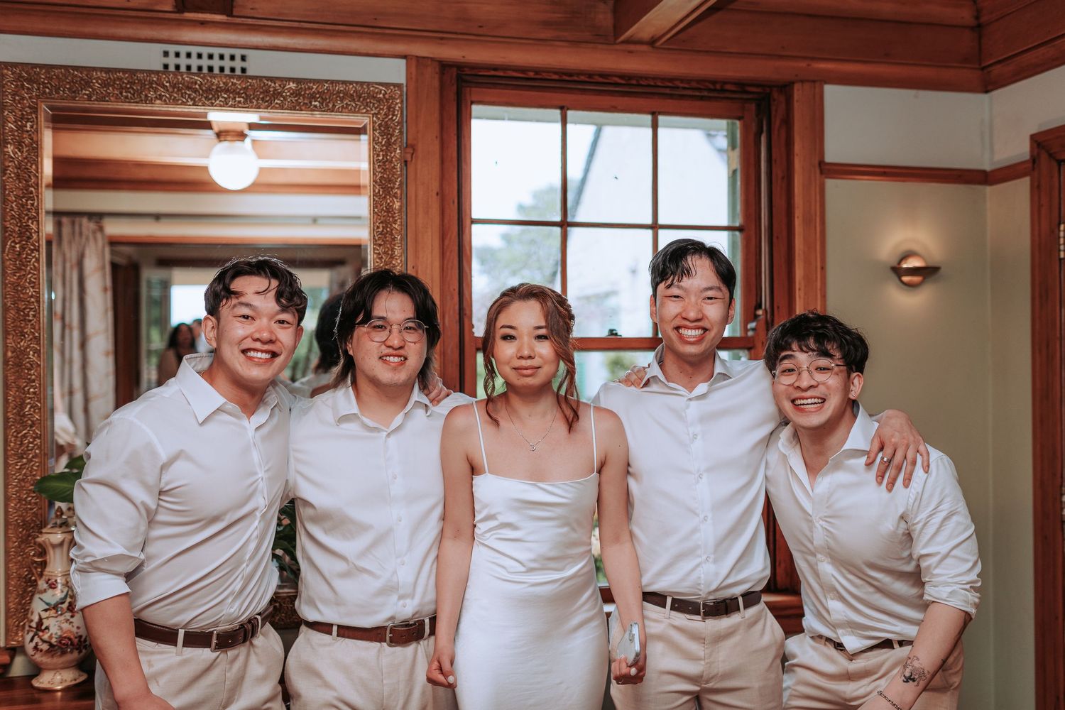 Wedding party poses indoors with wooden paneling and natural light.