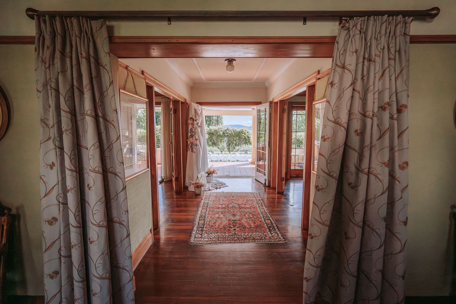 A welcoming hallway with wooden floors and floral curtains leads to a bright window view.