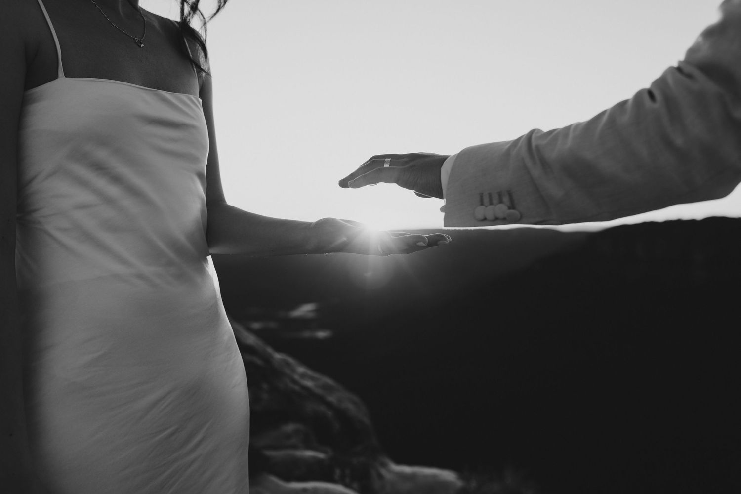 Artistic black and white silhouette of hands reaching toward sunlight.