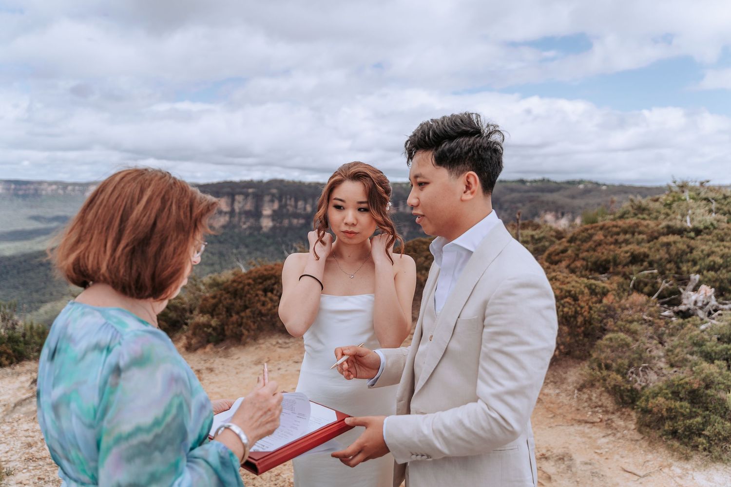 An intimate ceremony takes place on a clifftop overlooking a dramatic mountain valley.