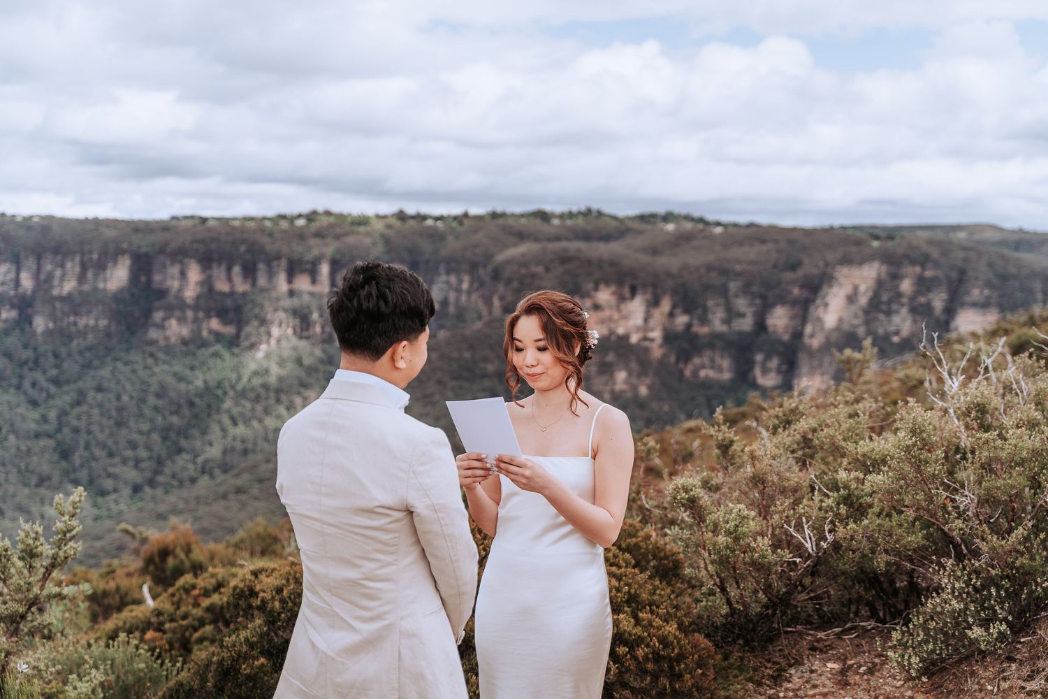 A couple exchanges vows on a mountain cliff edge with dramatic valley views below.