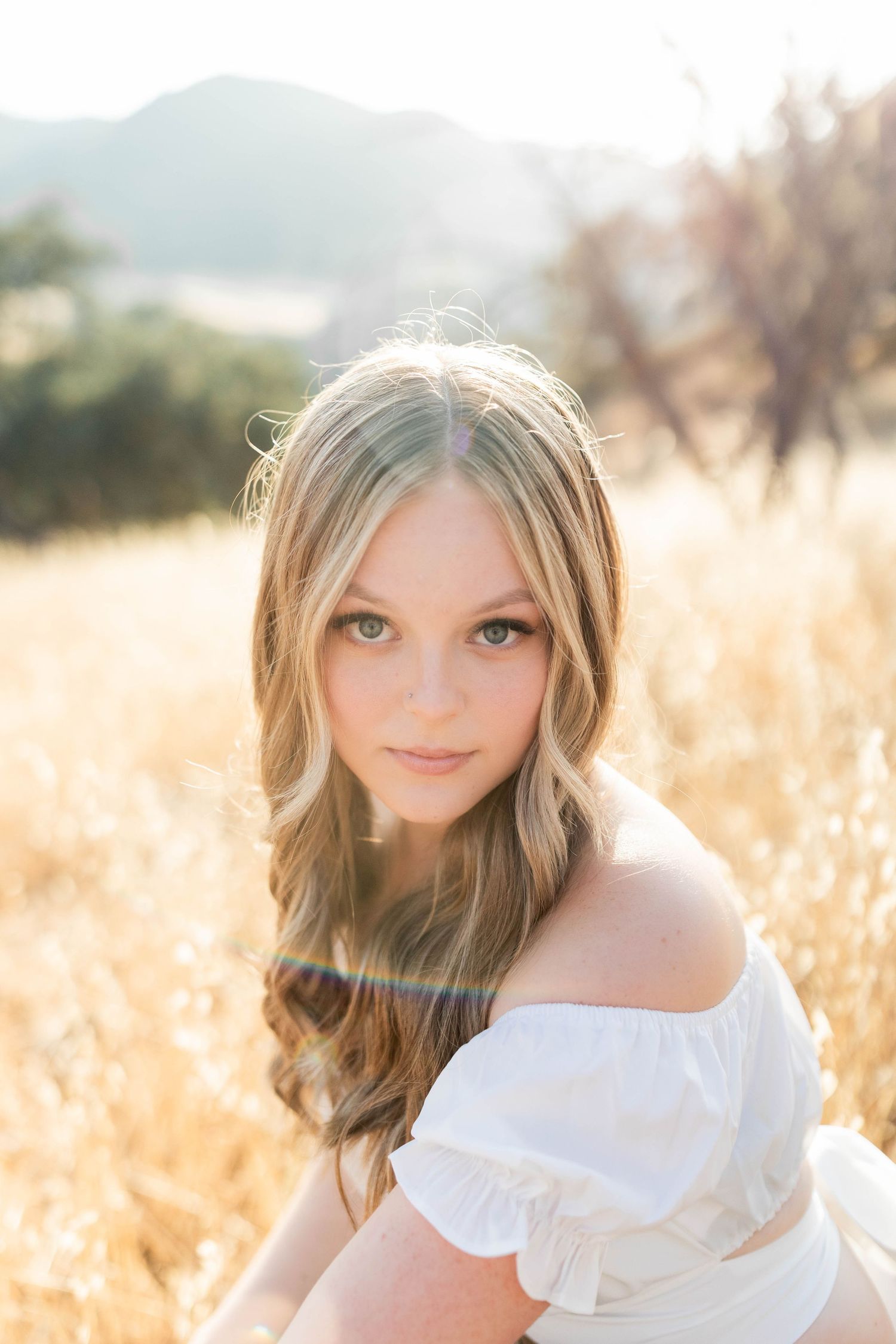 Dreamy outdoor portrait session in a field wearing a white ruffled top with soft lighting.