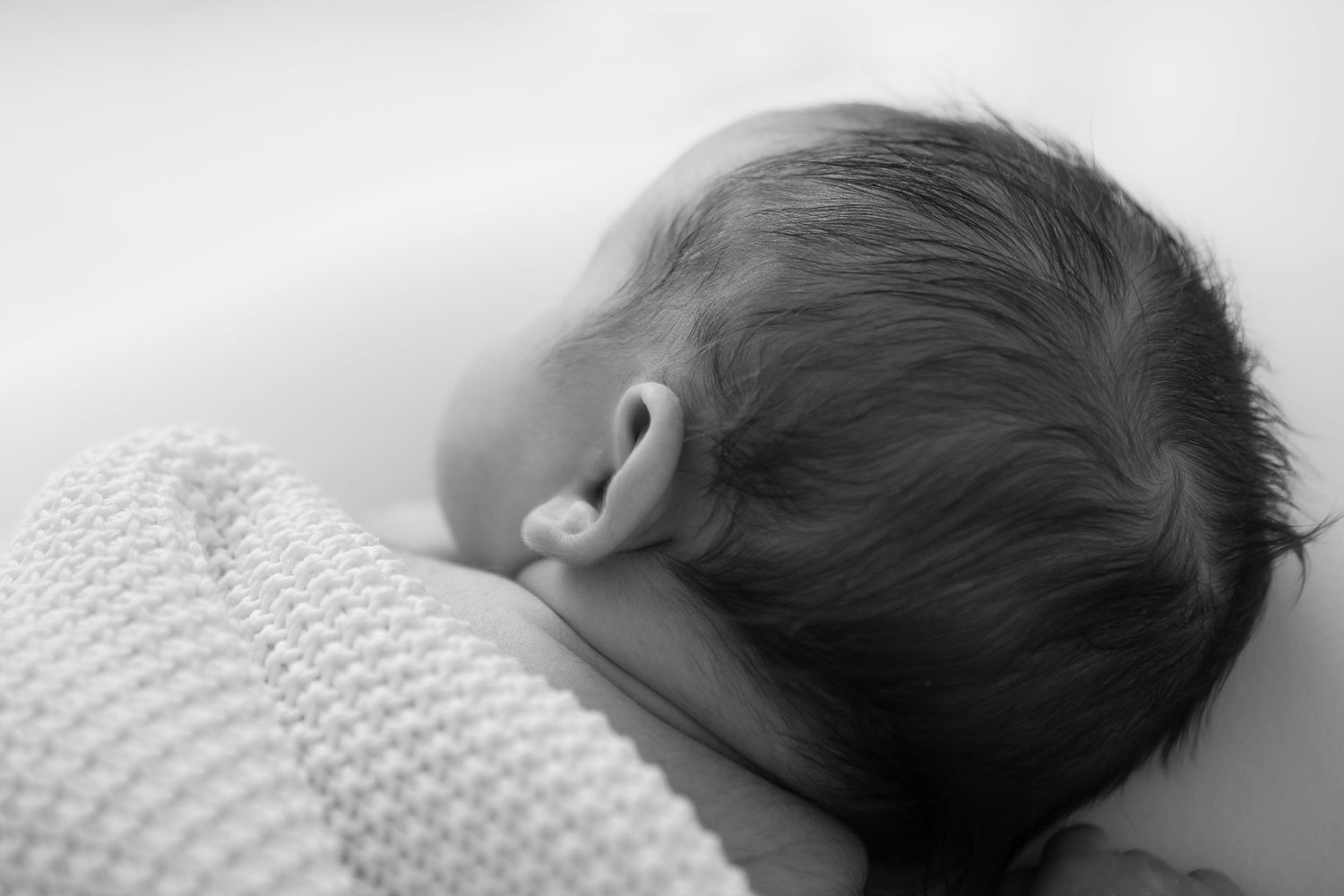Side view of sleeping newborn wrapped in white knit blanket.