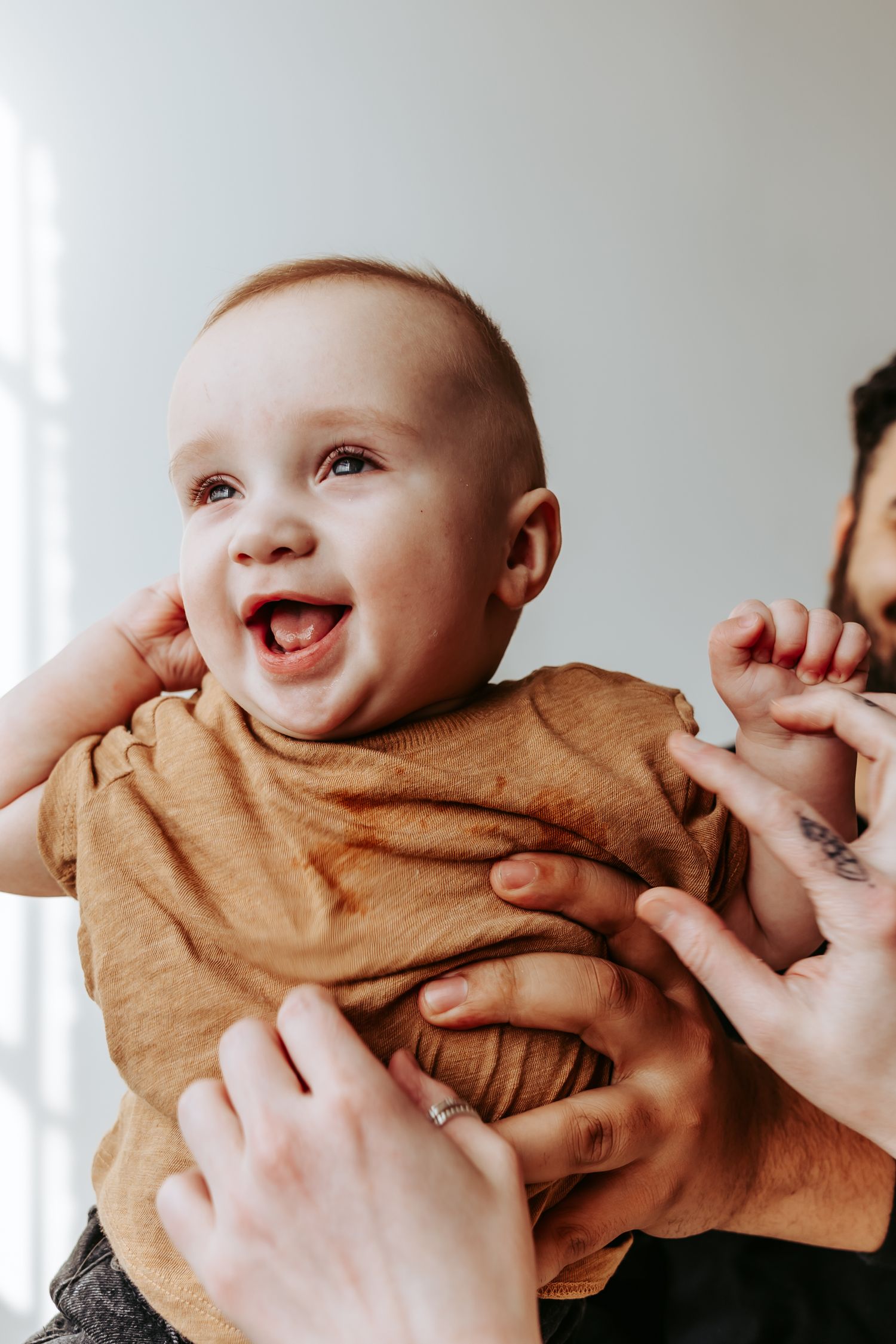 Smiling baby in brown outfit being held up with joyful expression.