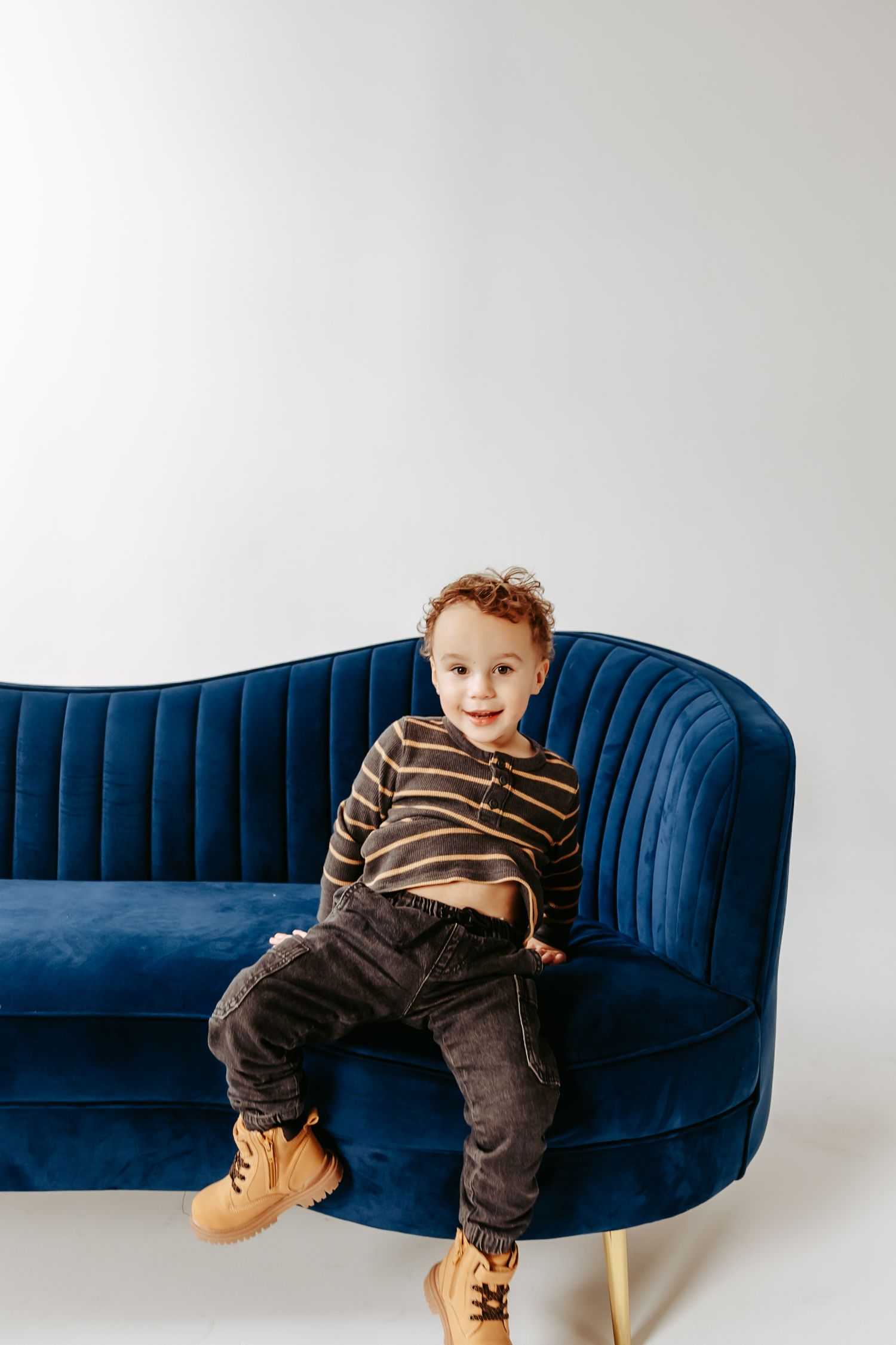 Young child in striped shirt sitting casually on blue velvet couch.