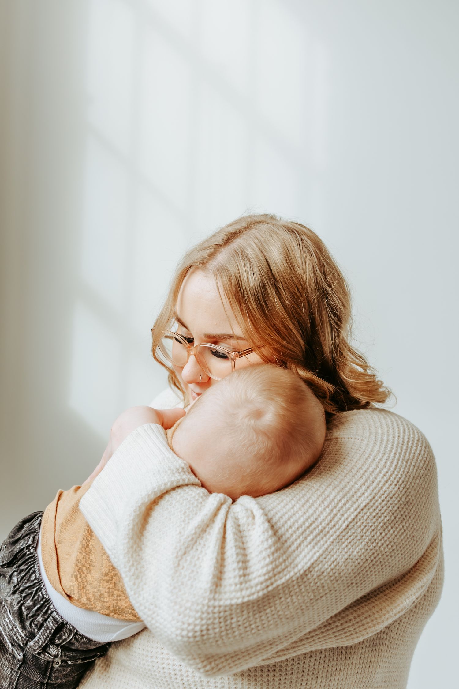 Parent in cream sweater holding sleeping baby in tender embrace.