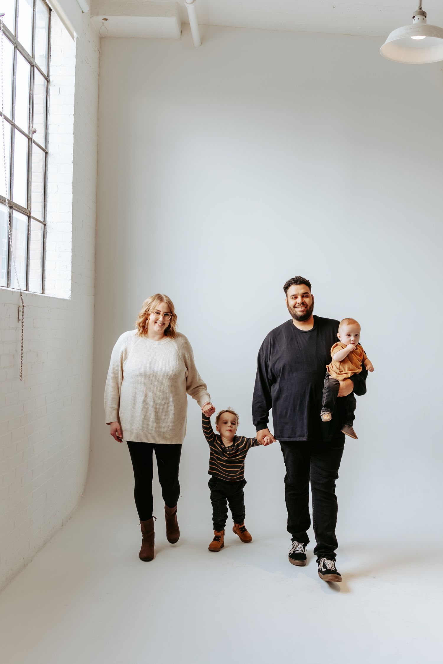 Young family walking together in white studio setting.