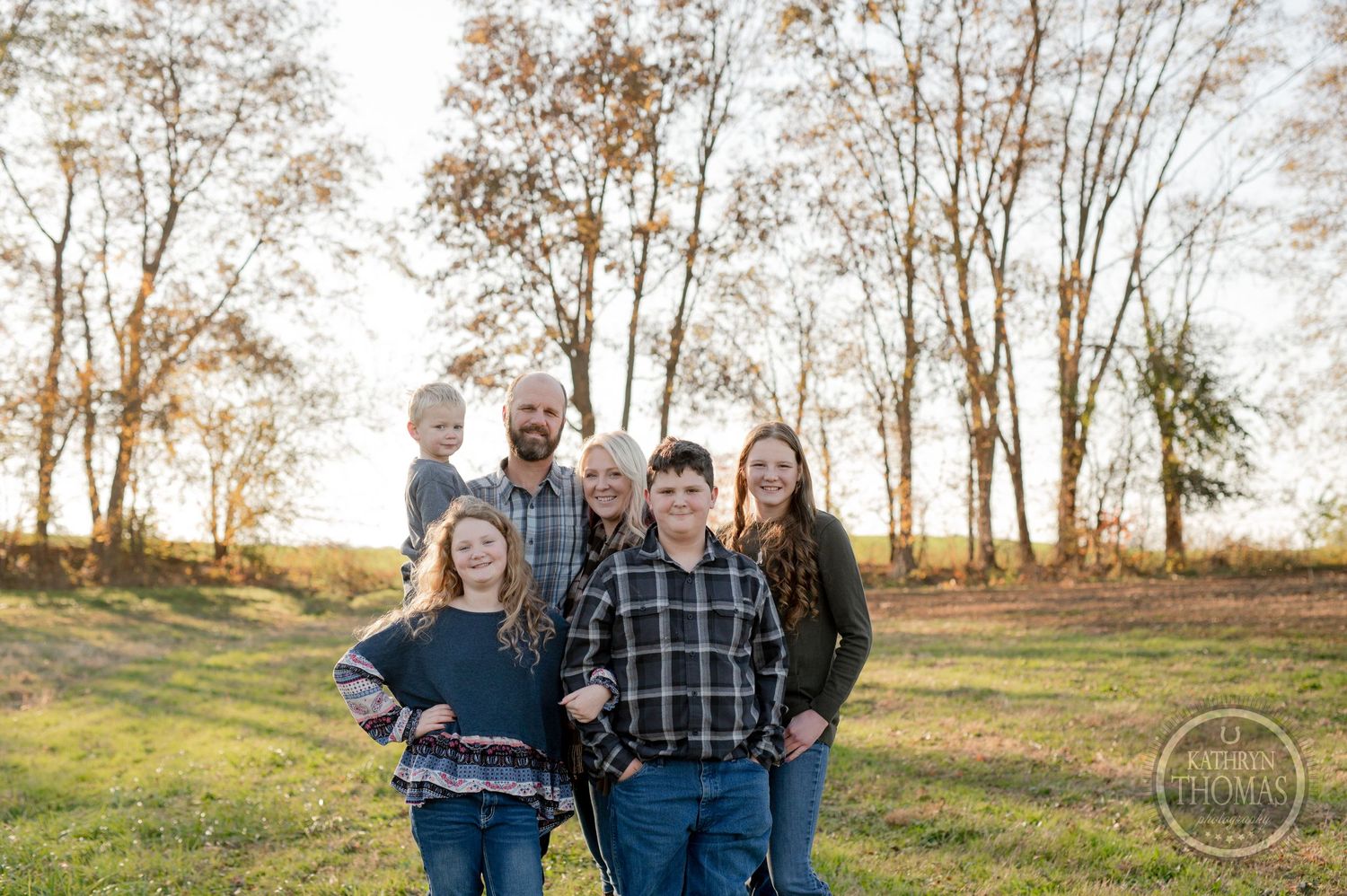 Family group portrait in casual wear against golden sunset and trees.