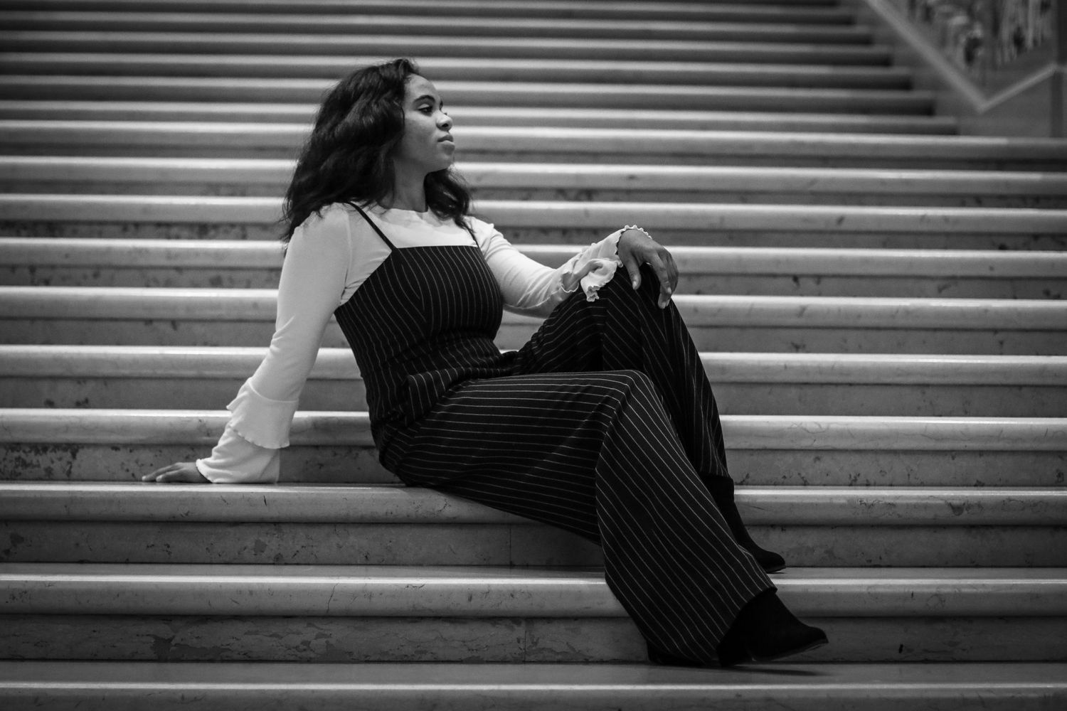 Artistic black and white photos of person sitting on grand marble stairs.