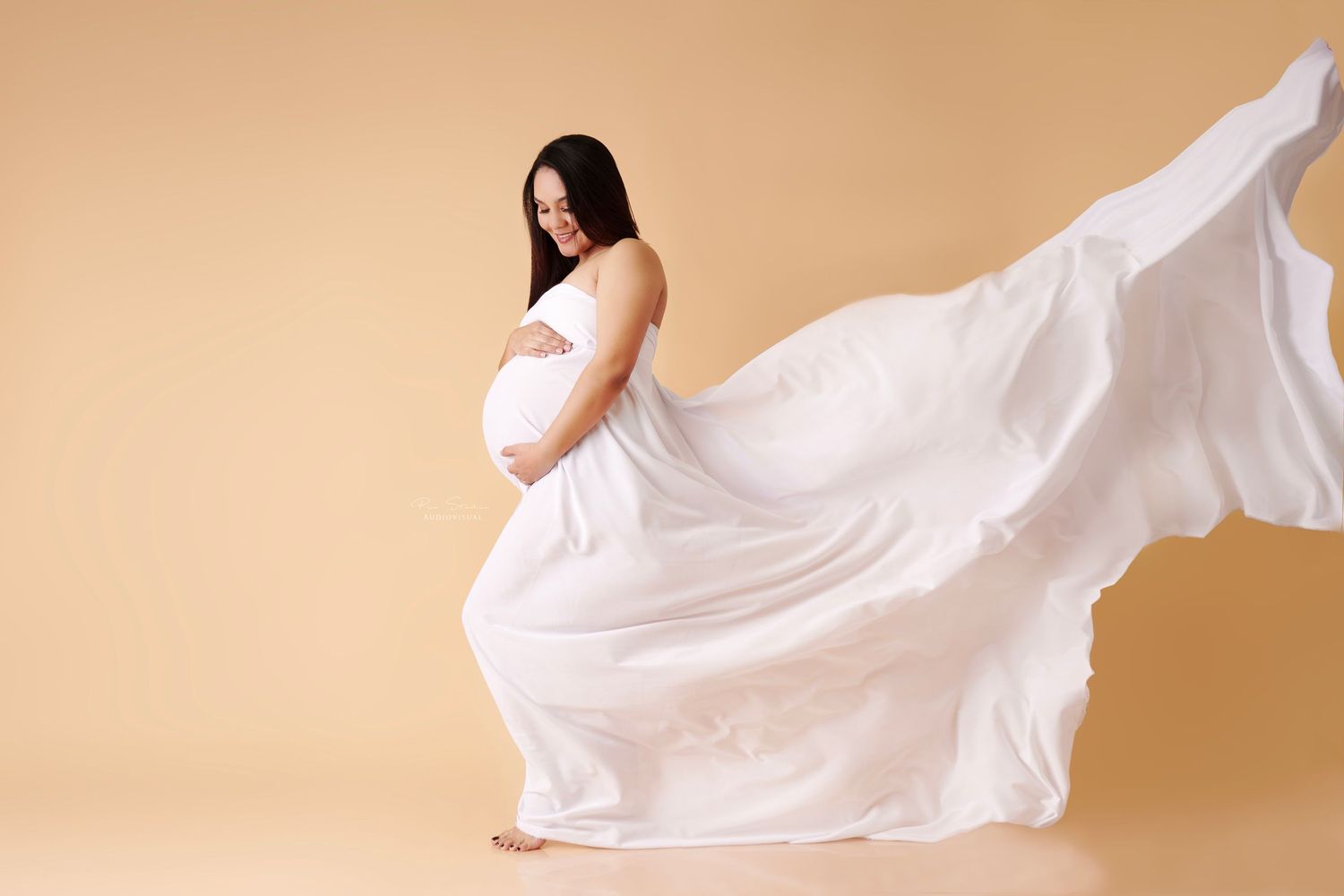 Mom-to-be cradling su barriga en una sesión de maternidad, wearing a flowing dress, in a scenic outdoor location flying dress tela voladora