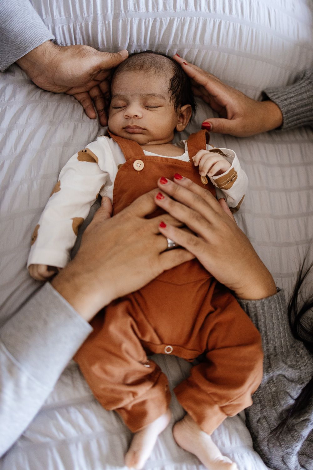 Parents put their hands on their sleeping baby during newborn photo shoot