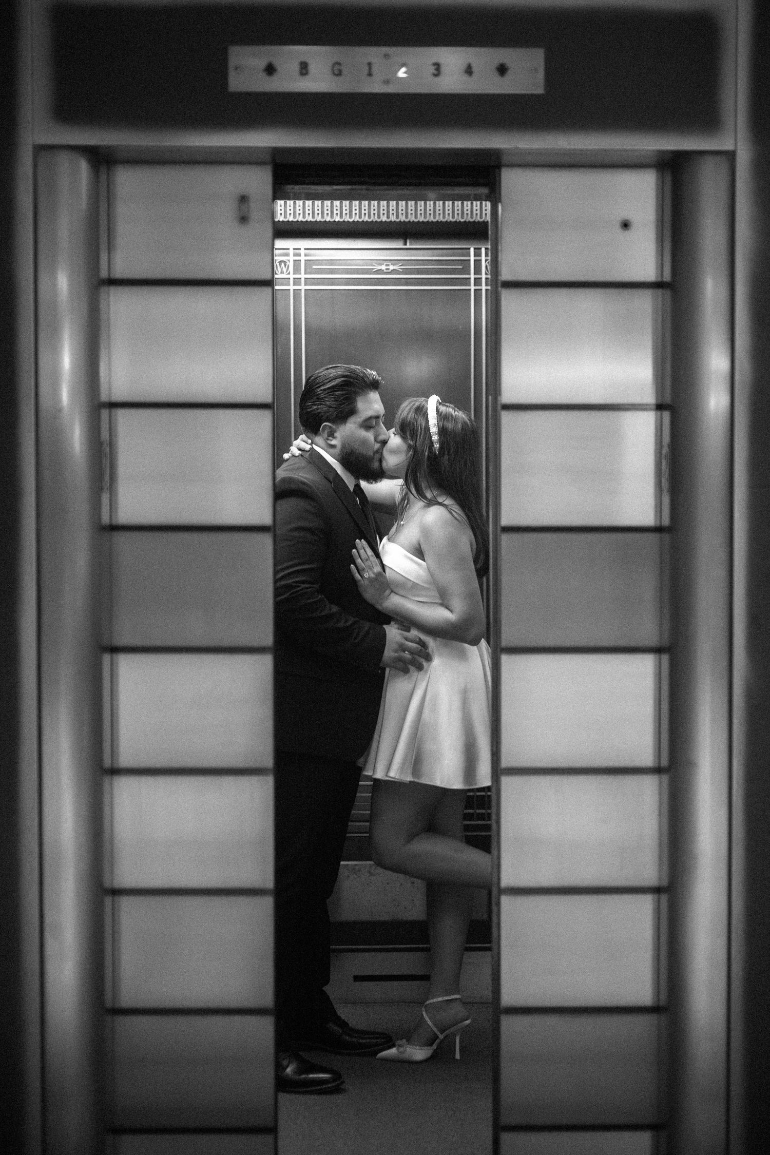 A romantic black and white photograph of a couple sharing an intimate moment inside an elevator.