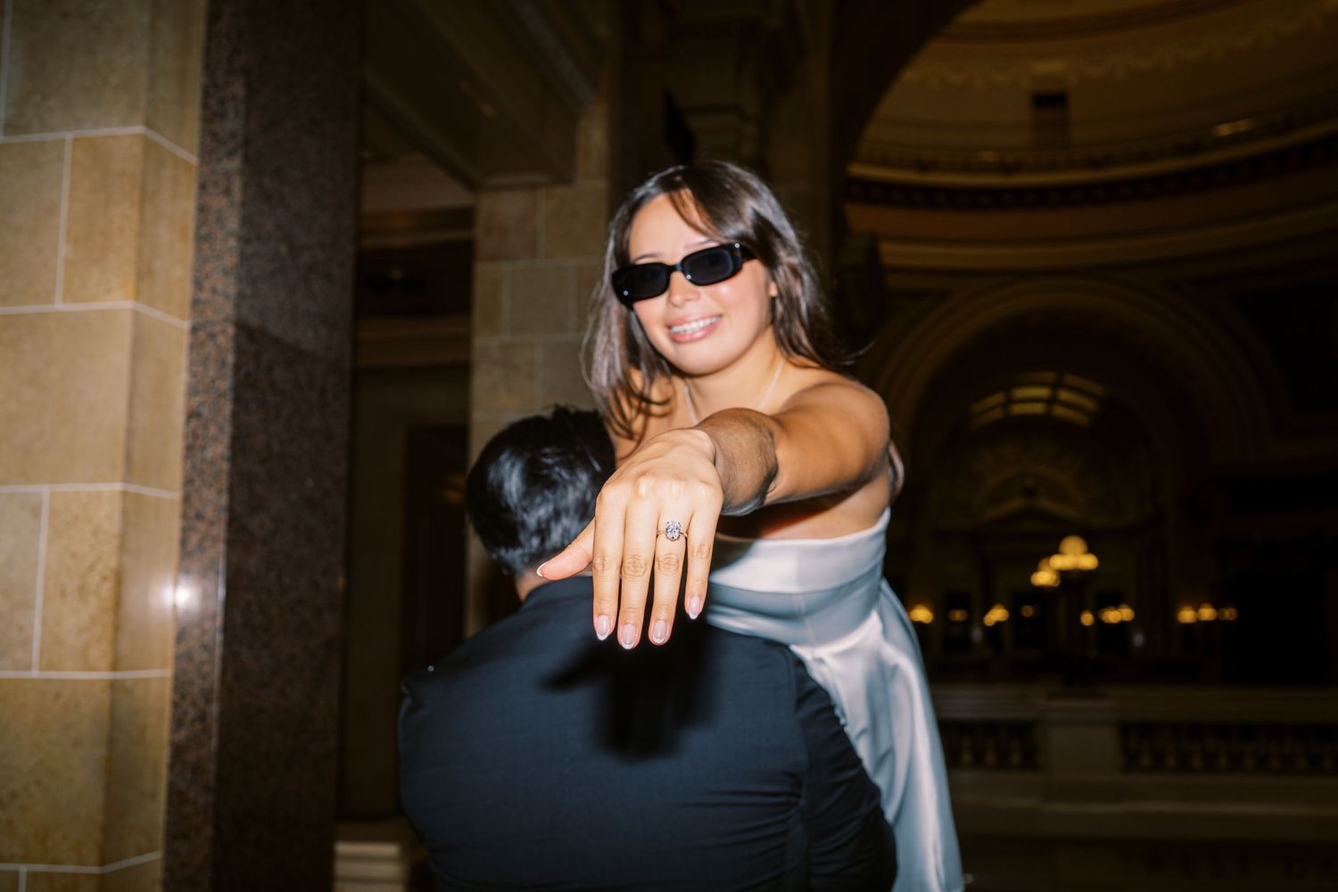 Person in silver dress and sunglasses poses in front of ornate building interior at night.