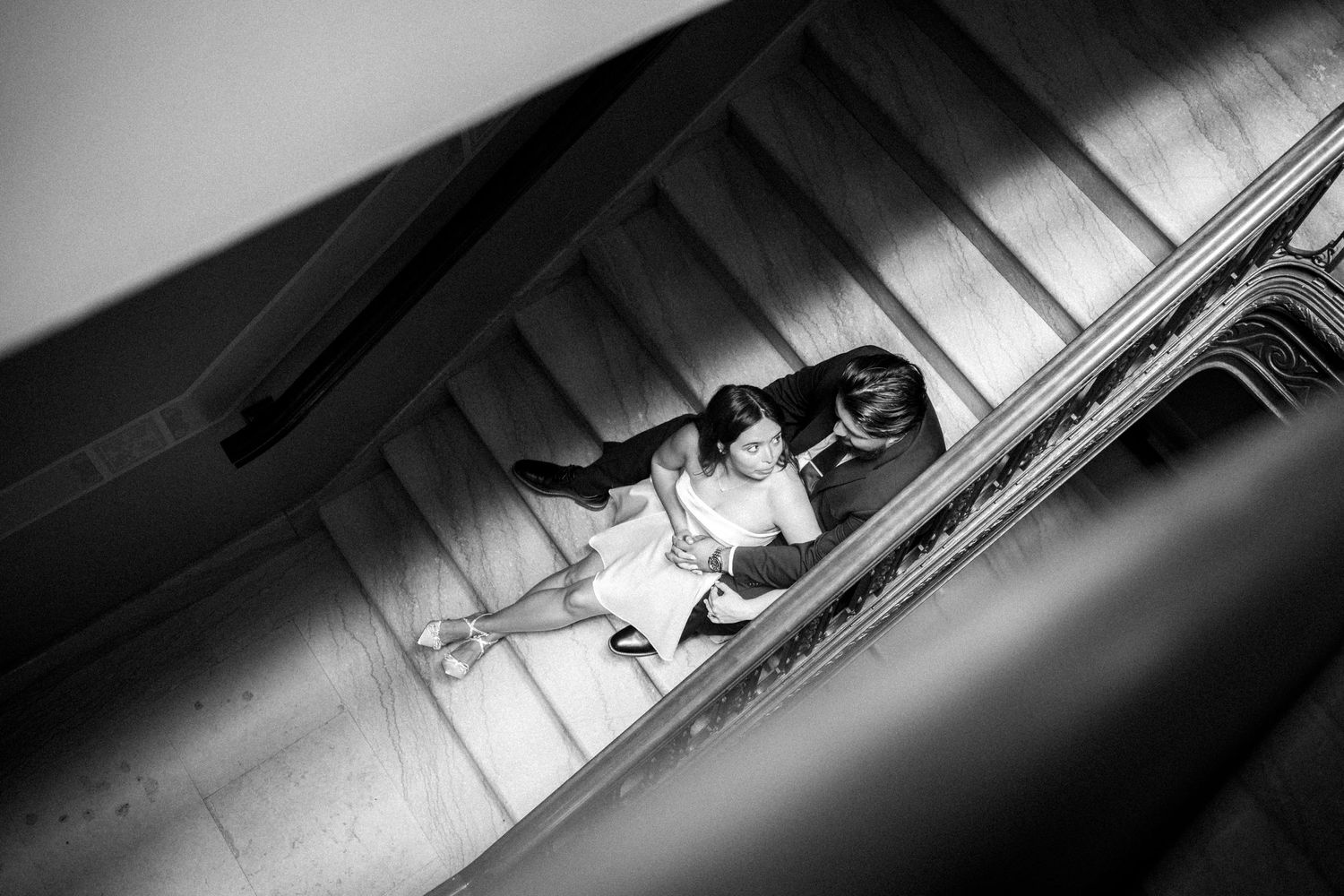A black and white photo looking down a stairwell shows people sitting on the steps in dramatic shadows.