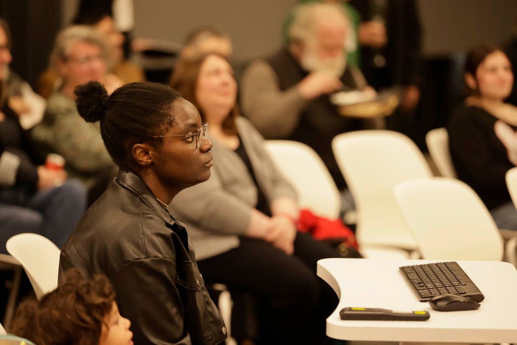 Conference attendee sitting in white chair with laptop during presentation.