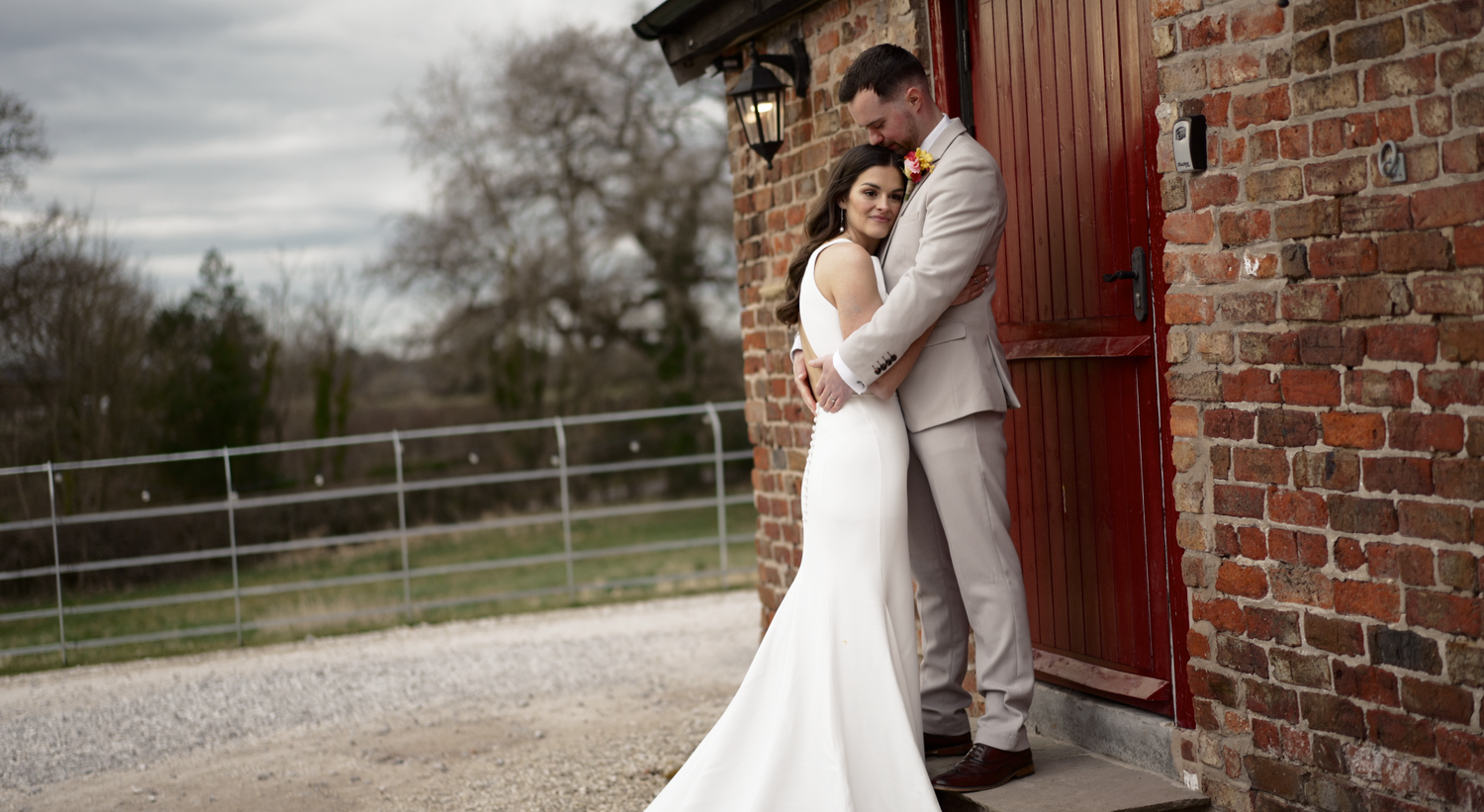 Romantic couple in wedding attire posing against rustic red barn door.