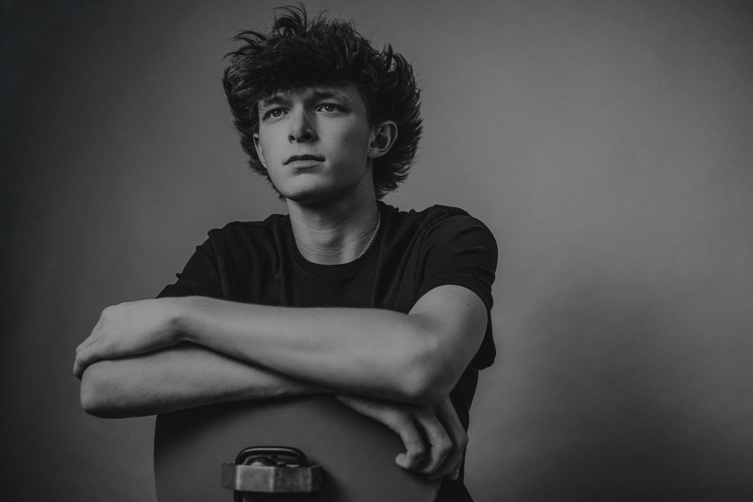 Dramatic black and white portrait against a dark background showing crossed arms and messy hair.