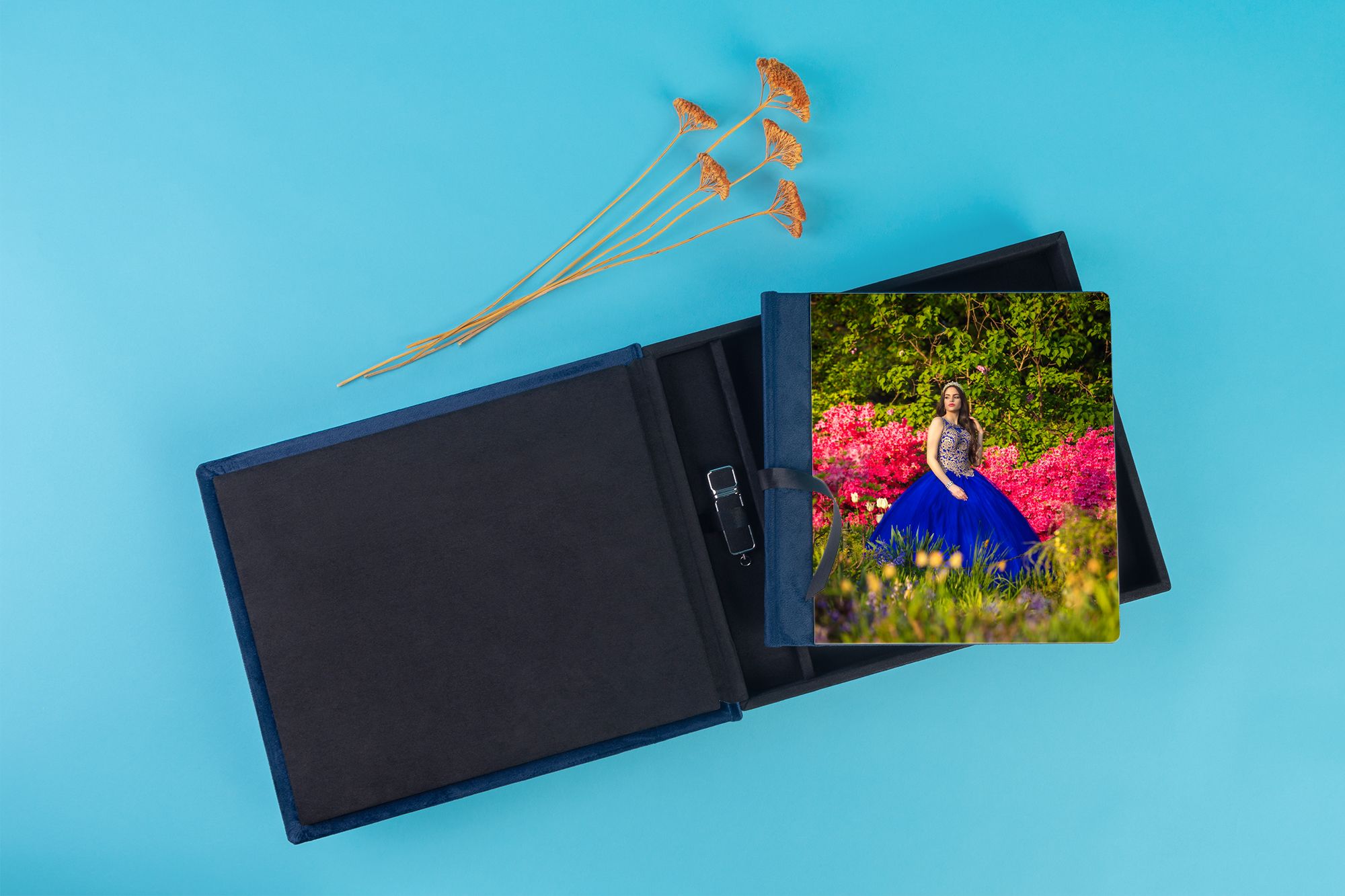 Black photo album with dried flowers and colorful print on blue background.